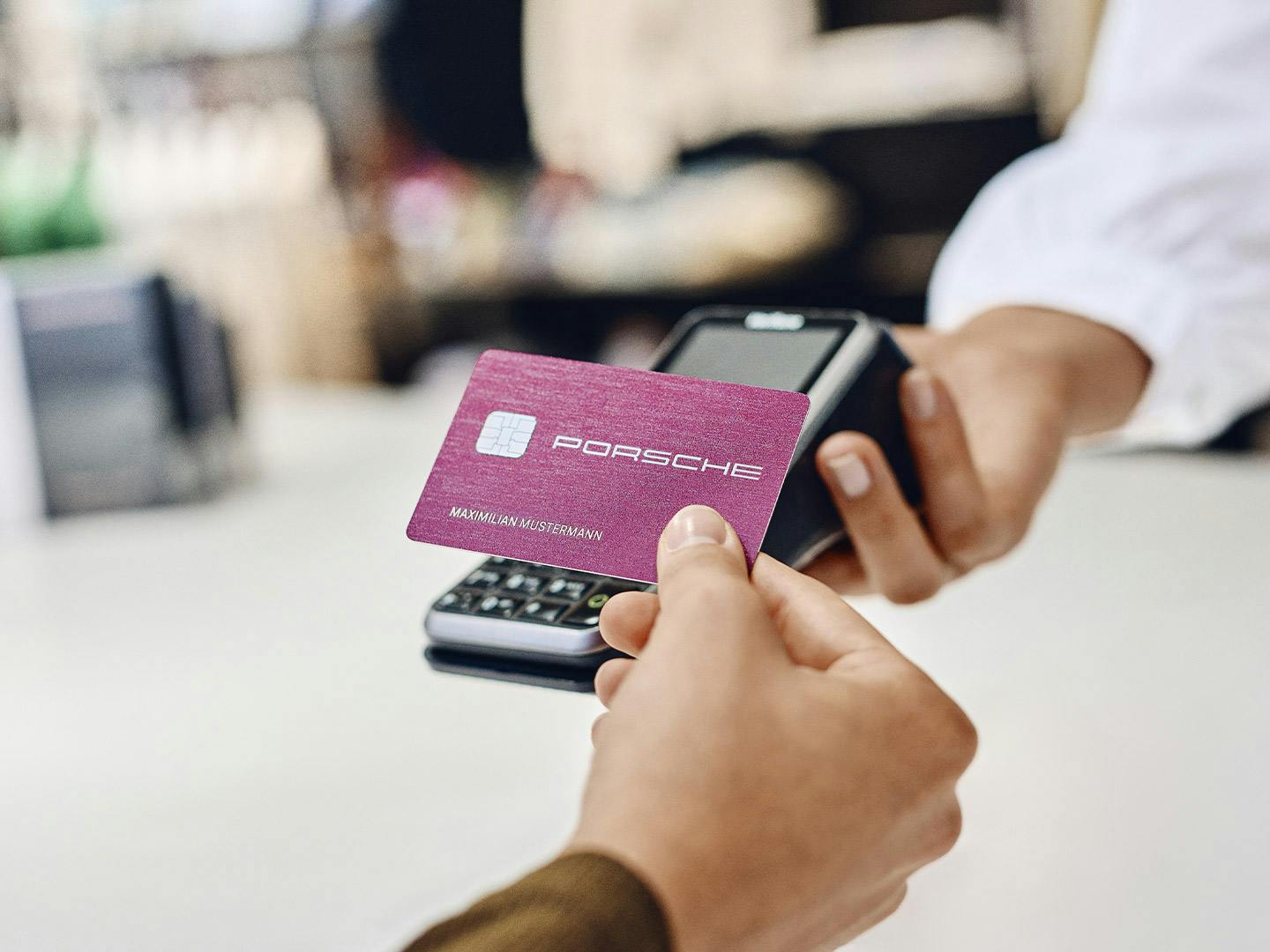 Die Porsche Card in der Farbe Sternrubin Neo wird an der Kasse an ein Kartenlesegerät gehalten.