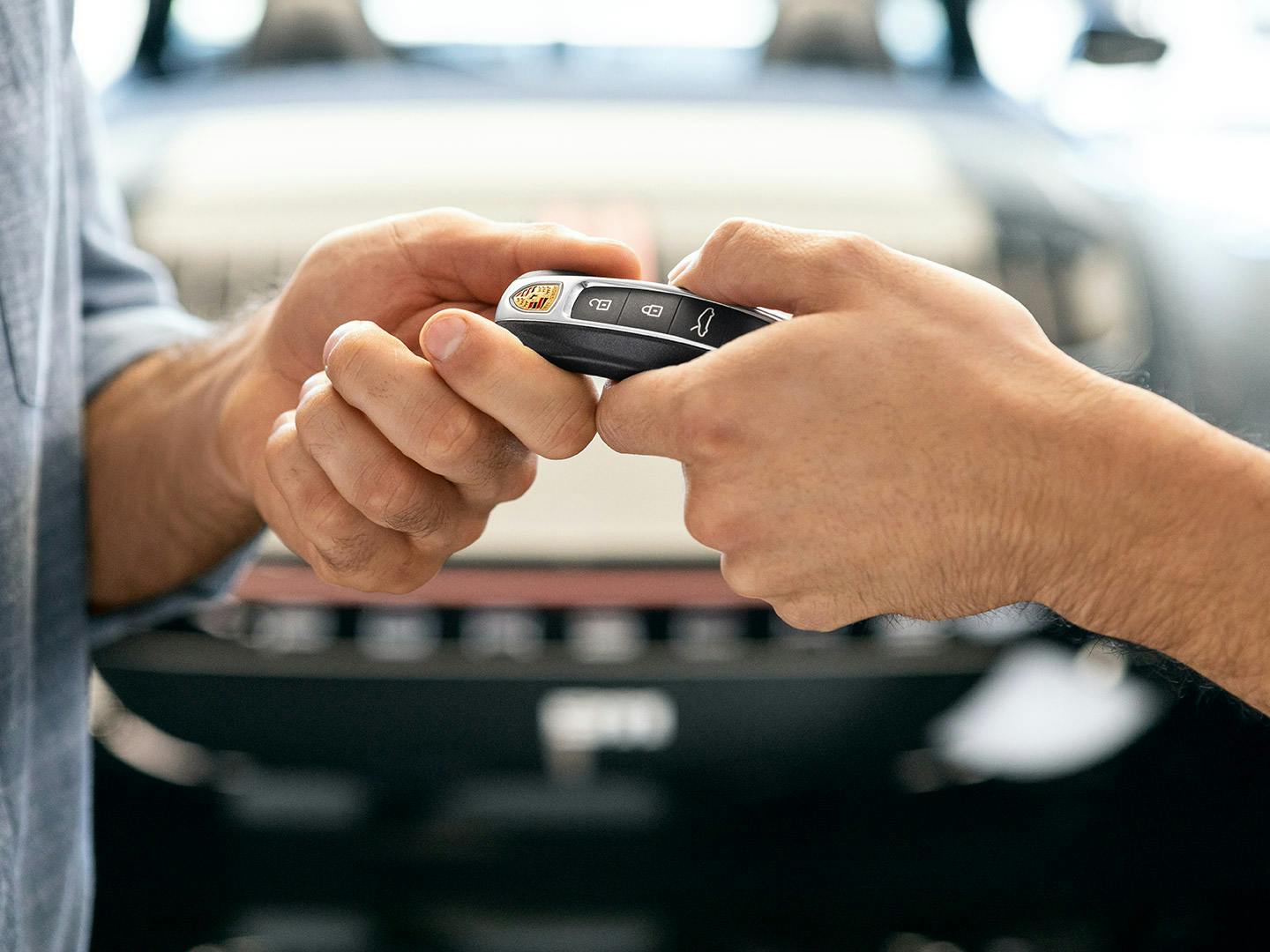 On y voit deux mains remettant une clé de Porsche. Une voiture se trouve à l'arrière-plan.
