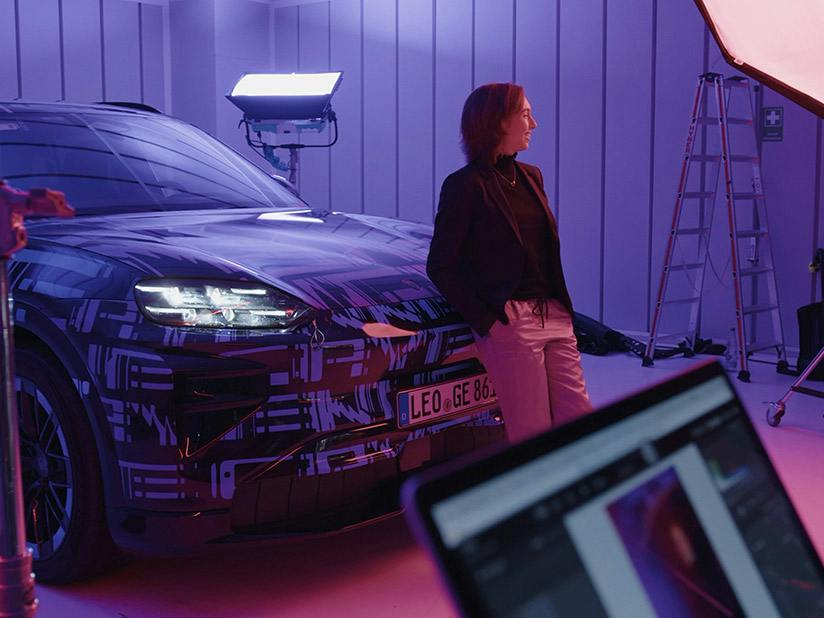 Porsche Mitarbeitern Viktoria steht vor einem getarnten Porsche Cayenne Turbo und macht sich bereit für eine Fotoaufnahme.