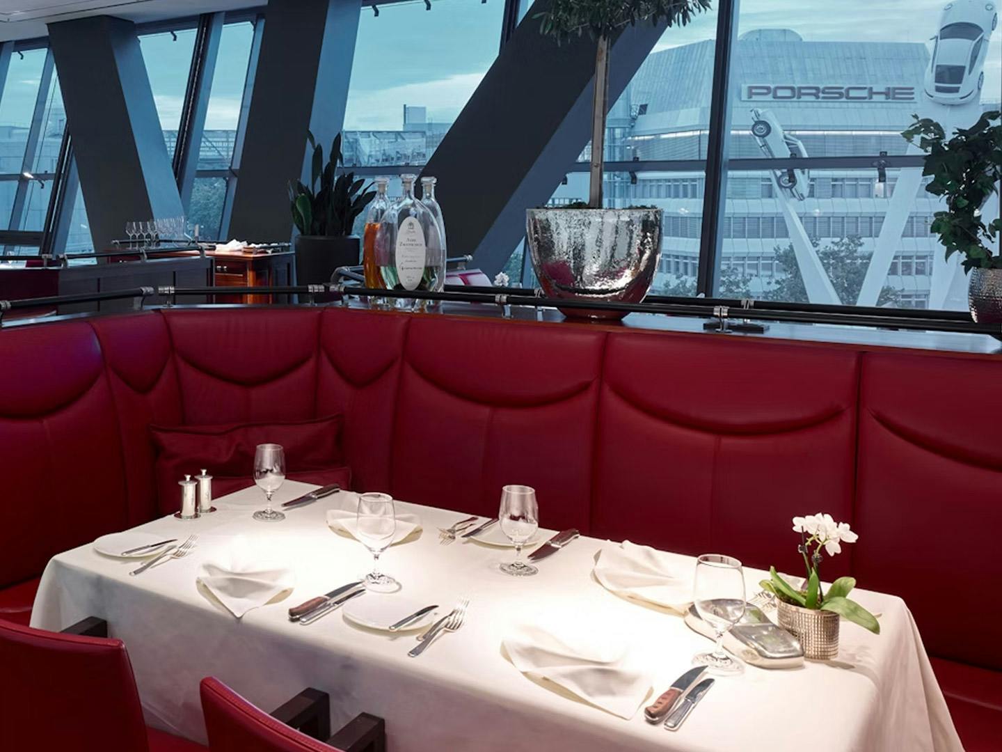 Das moderne Porsche Restaurant Christophorus mit roten gepolsterten Sitzecken. Das Gedeck ist akurat auf weissen Tischdecken angerichtet.