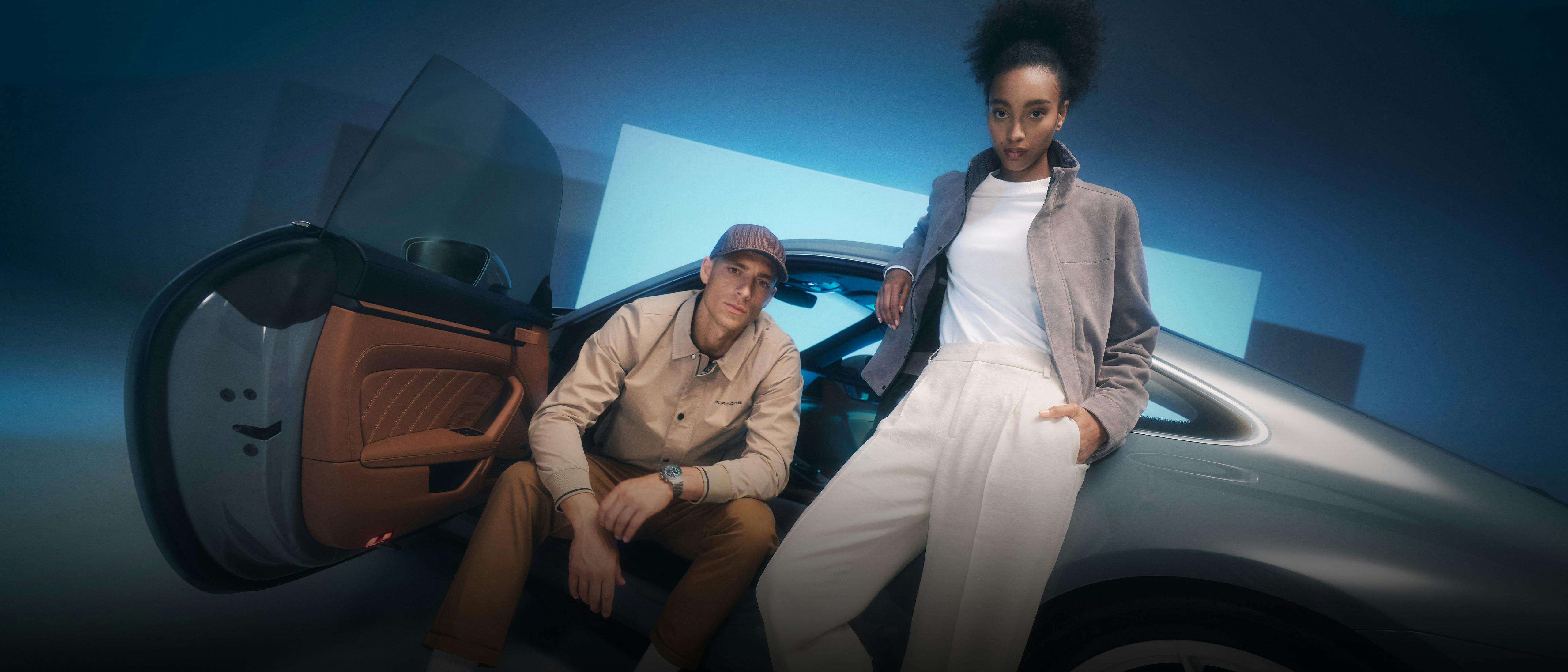 A man and a woman sit in front of a Porsche 911, facing the viewer.