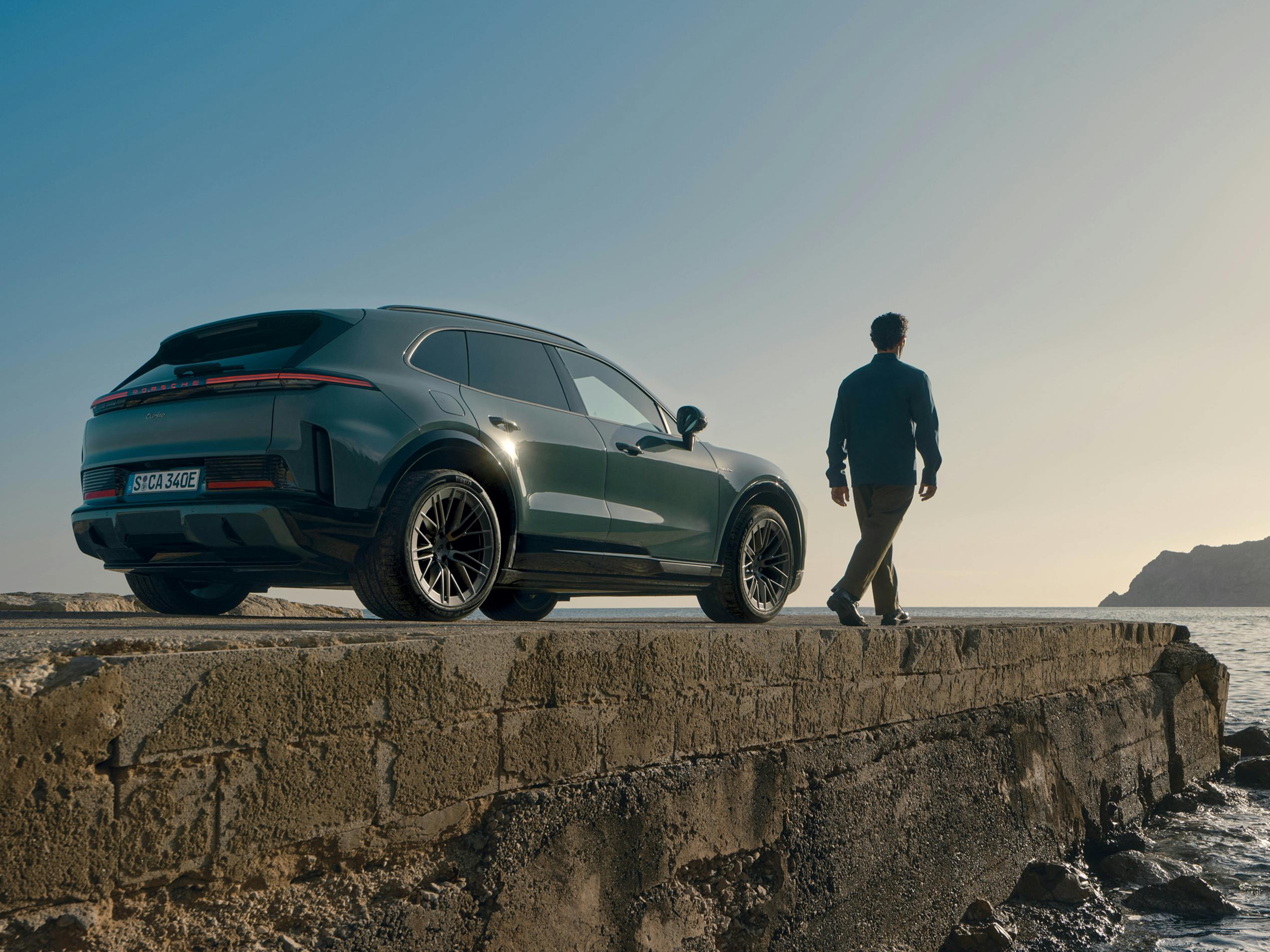 Un Porsche Macan y un Porsche Macan 4S circulan uno al lado del otro por una carretera que atraviesa un paisaje montañoso.