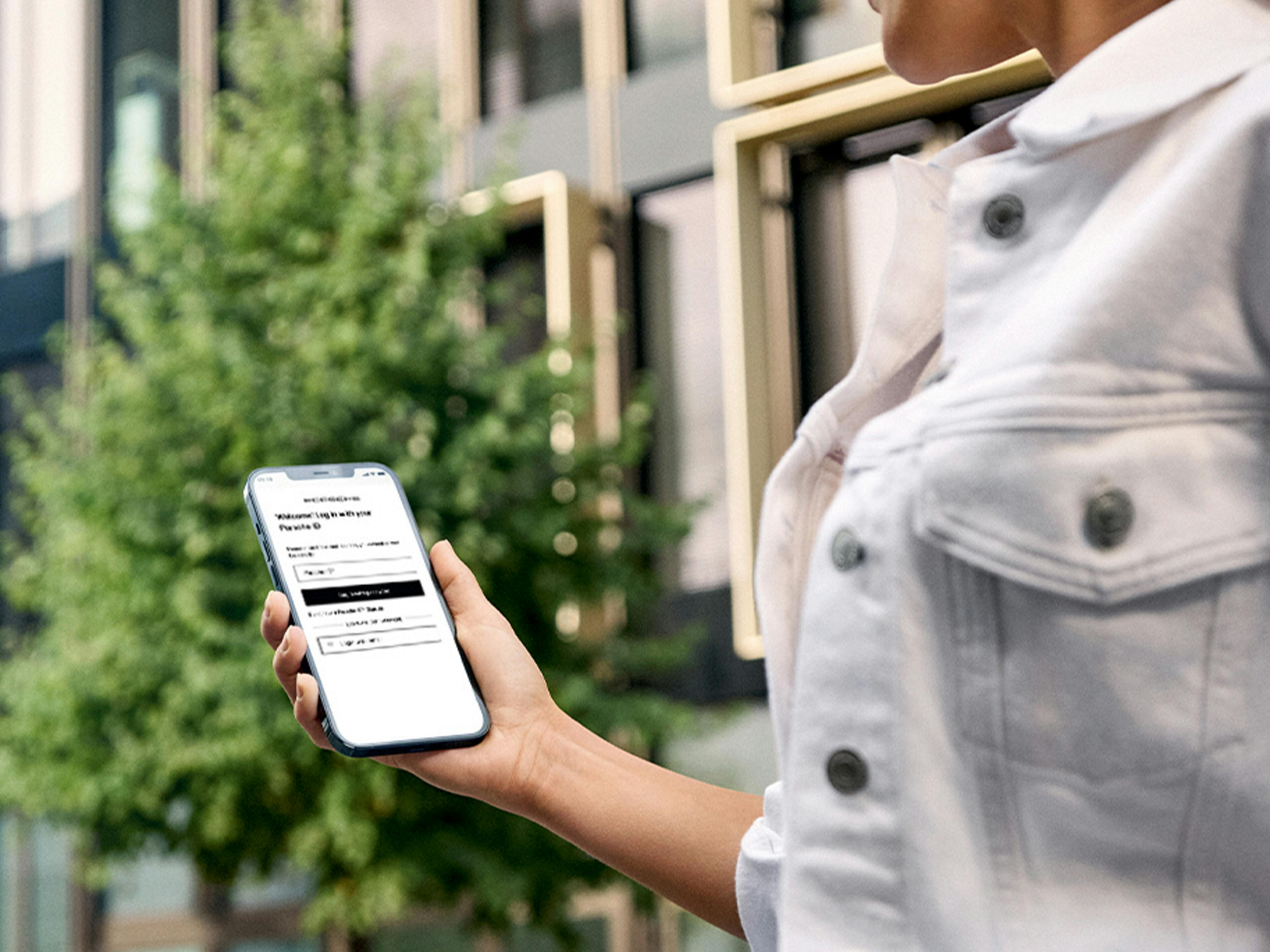 A person holding a smartphone outdoors, displaying My Porsche app.