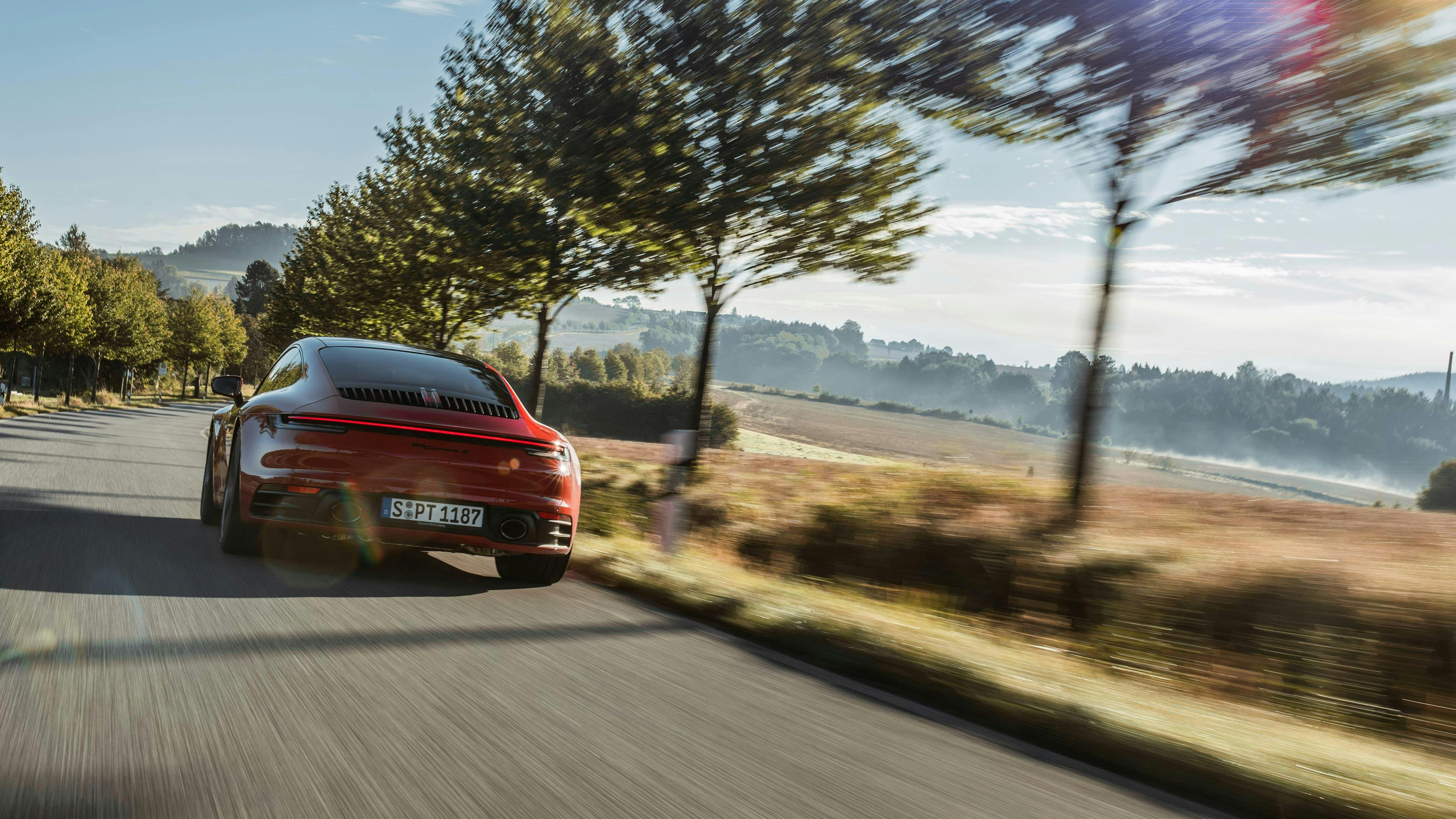 Red Porsche 911 Carrera S driving through landscape.