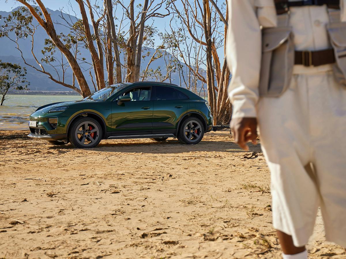 Um Porsche Macan 4S numa zona arenosa junto a algumas árvores. Um homem a caminhar em primeiro plano.