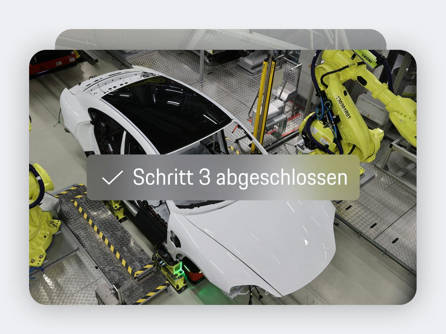 App-Ansicht mit Produktionsschritt: weiße Porsche-Karosserie auf dem Fließband mit gelben Roboterarmen und Text „Schritt 3 abgeschlossen“.