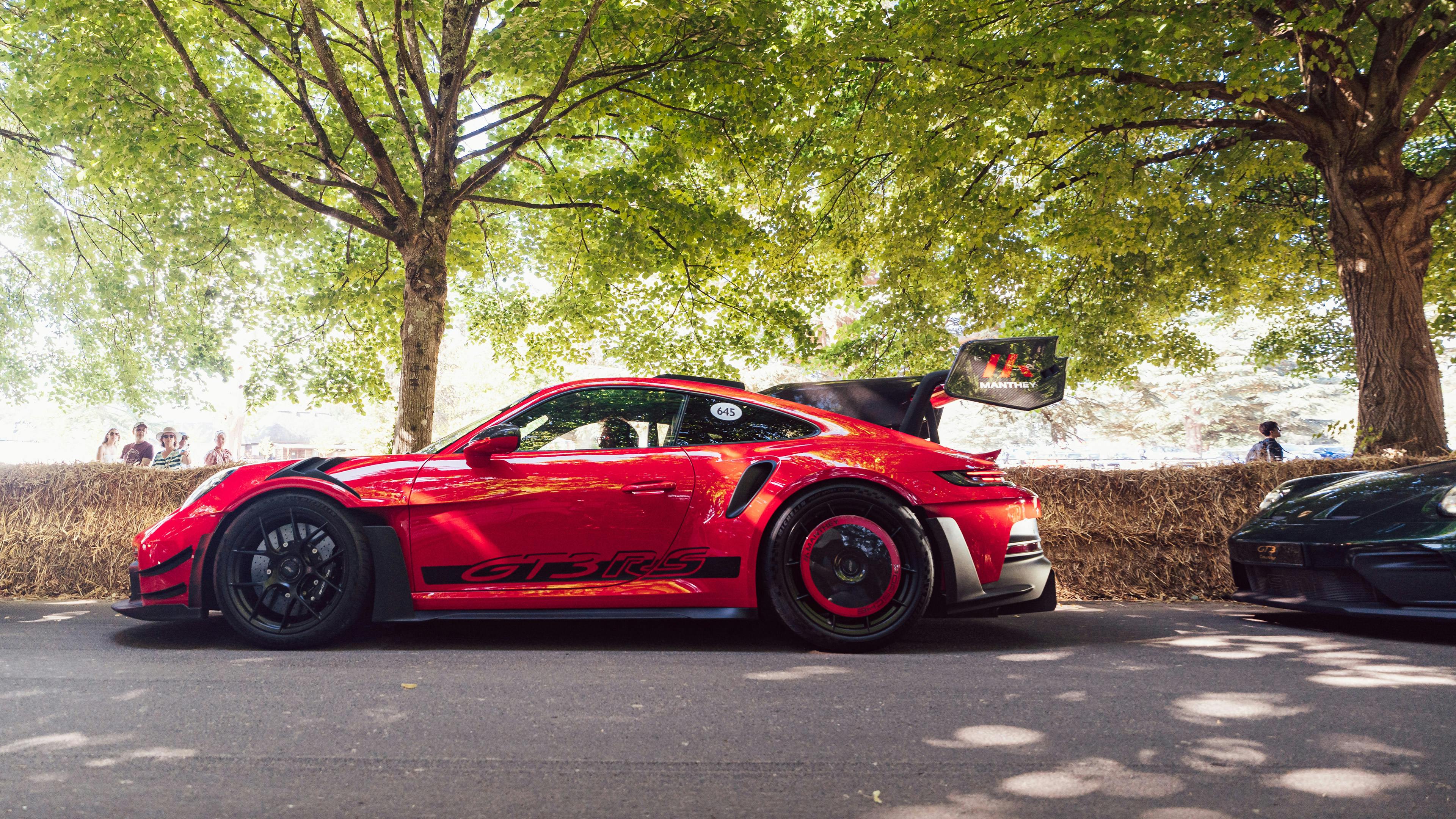 A red Porsche 911 GT3 RS with large rear wing parked on a tree-lined road at the Goodwood Festival of Speed.