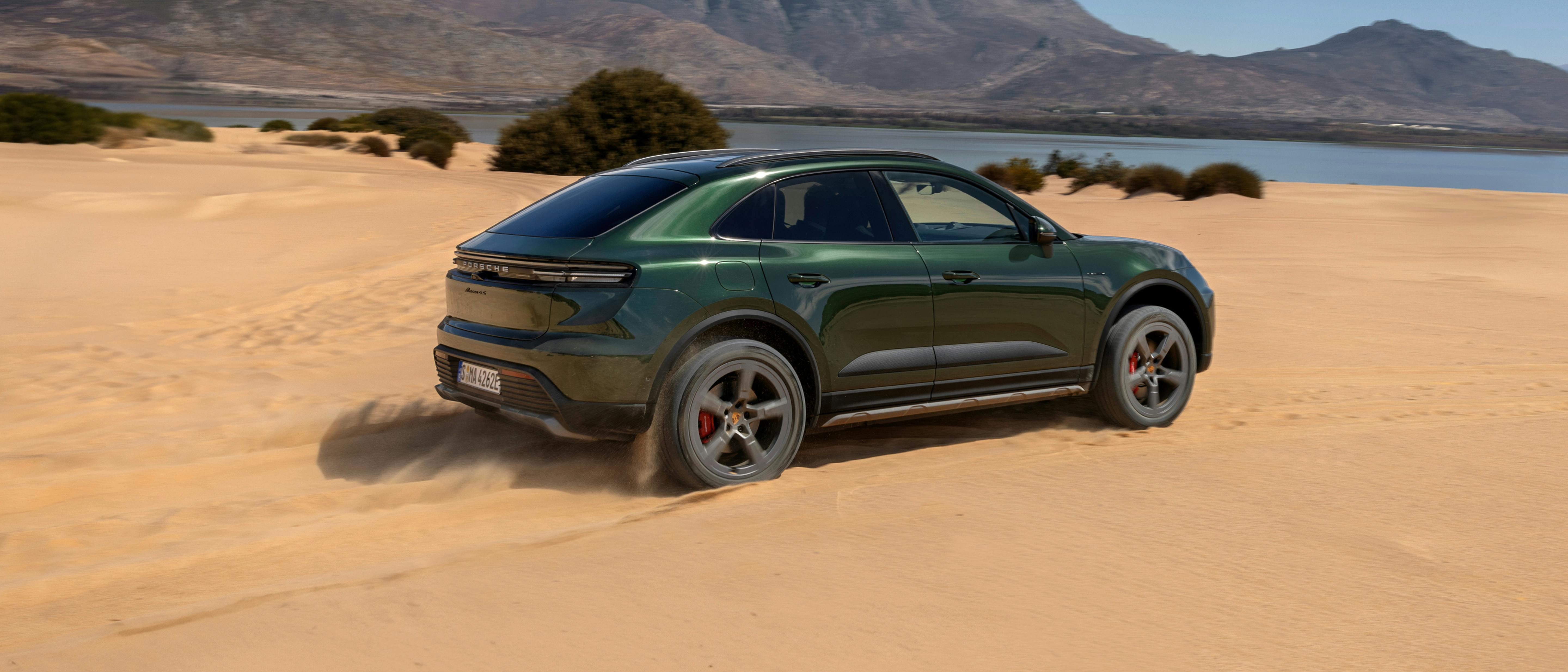 Um Porsche Macan 4S a circular sobre areia. Um lago e uma montanha ao fundo.