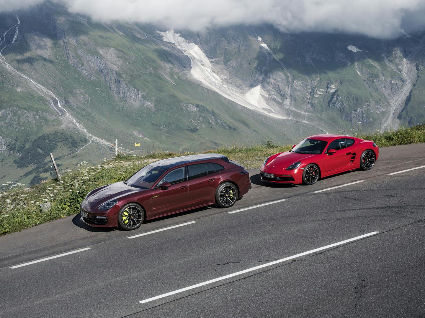 Twee rode Porsches staan geparkeerd aan de kant van de weg met bergen op de achtergrond