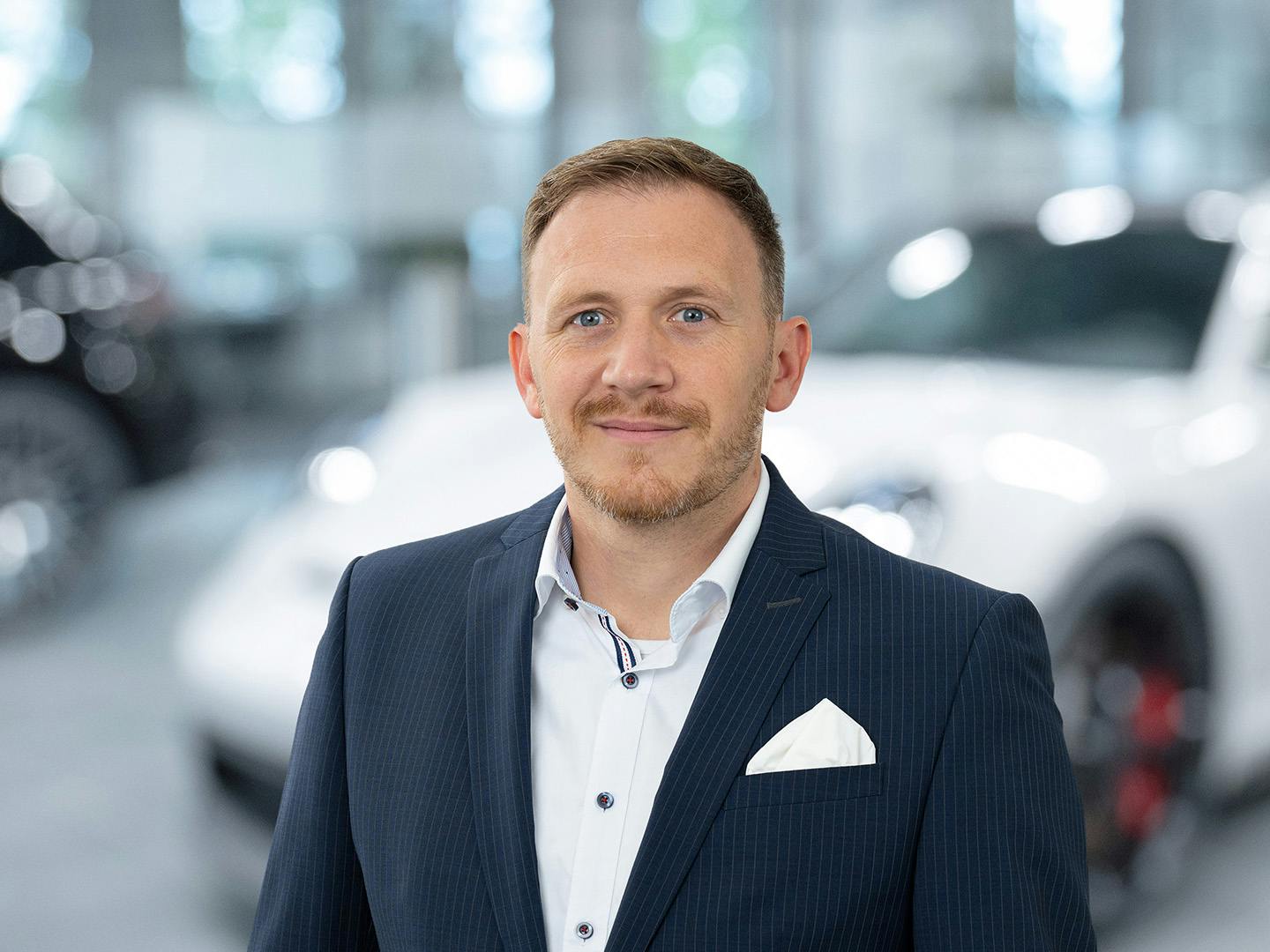 Porsche Mitarbeiterin berät einen Kunden der in einem Porsche Fahrzeug sitzt.