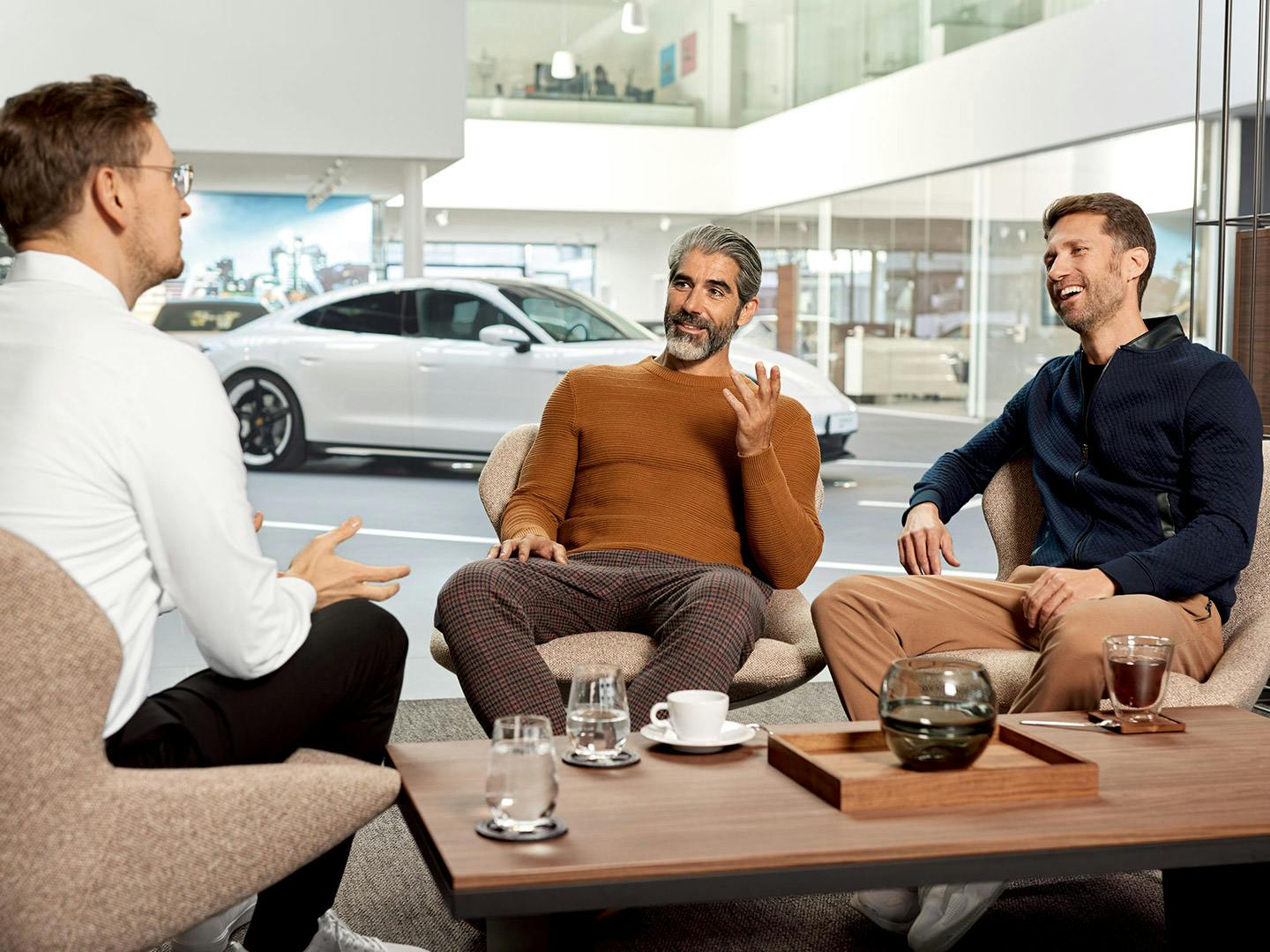 Two customers with Porsche employee sitting by a coffee table