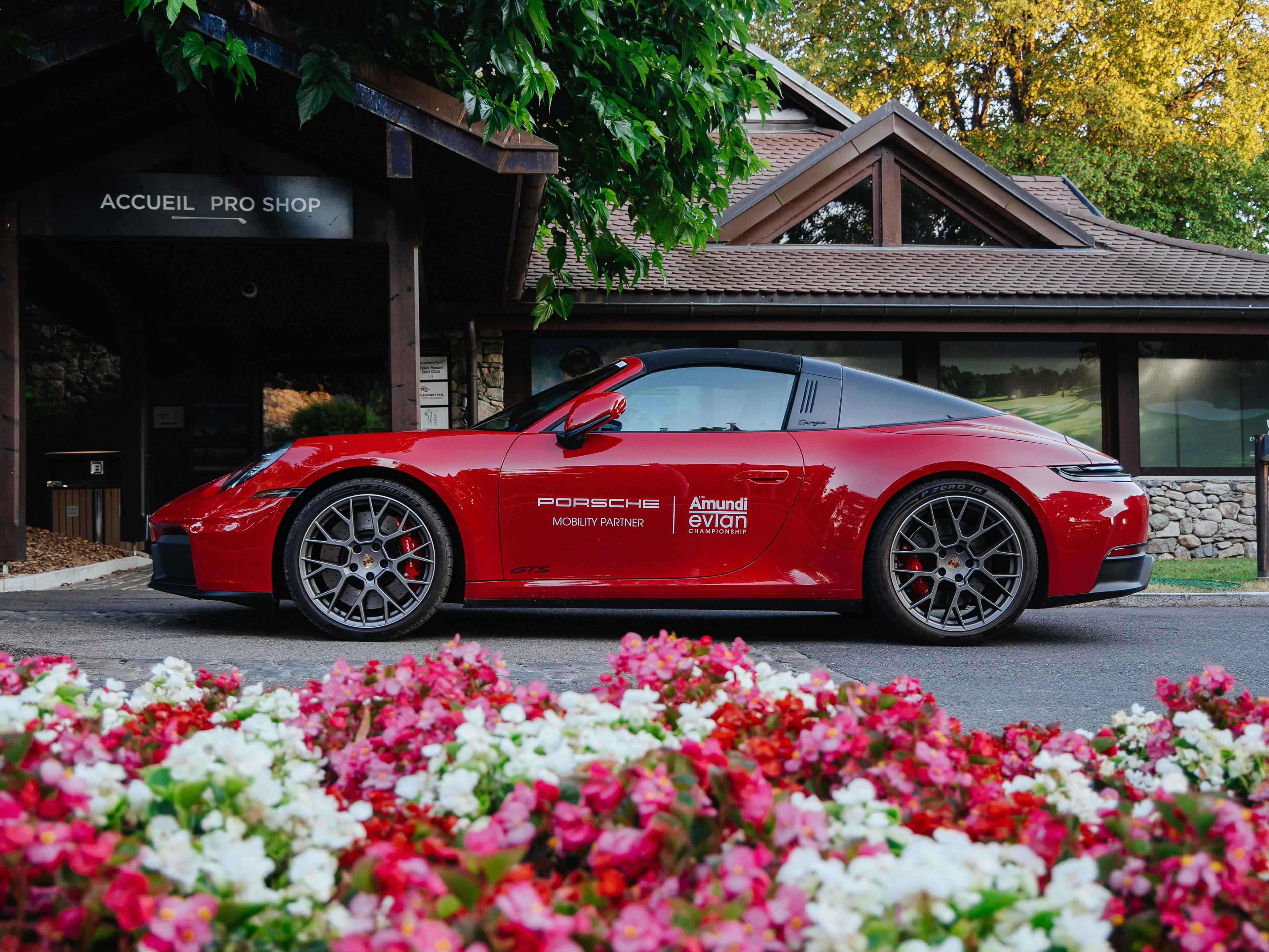 Roter Porsche 911 Targa GTS vor dem Golf-Clubhaus in Evian mit Blumenbeet im Vordergrund.