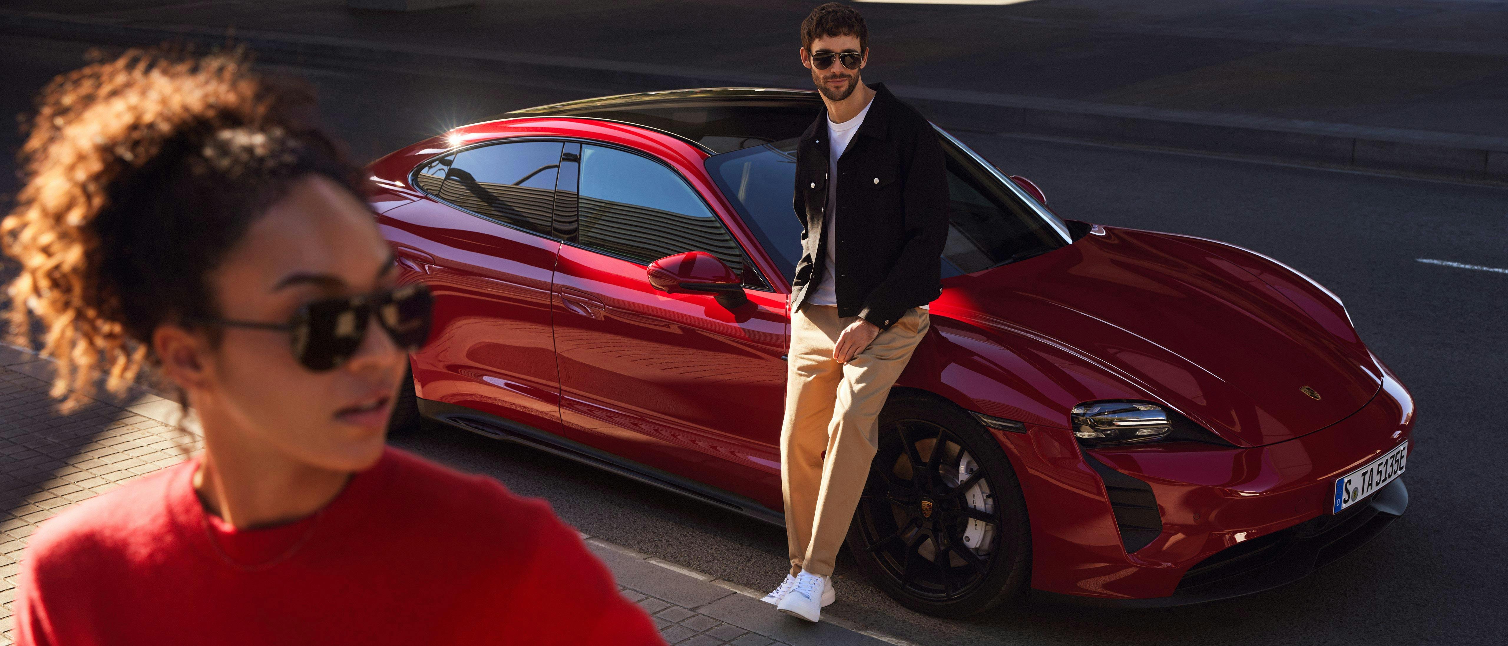 A woman and a man dressed elegantly, next to a Porsche Taycan.
