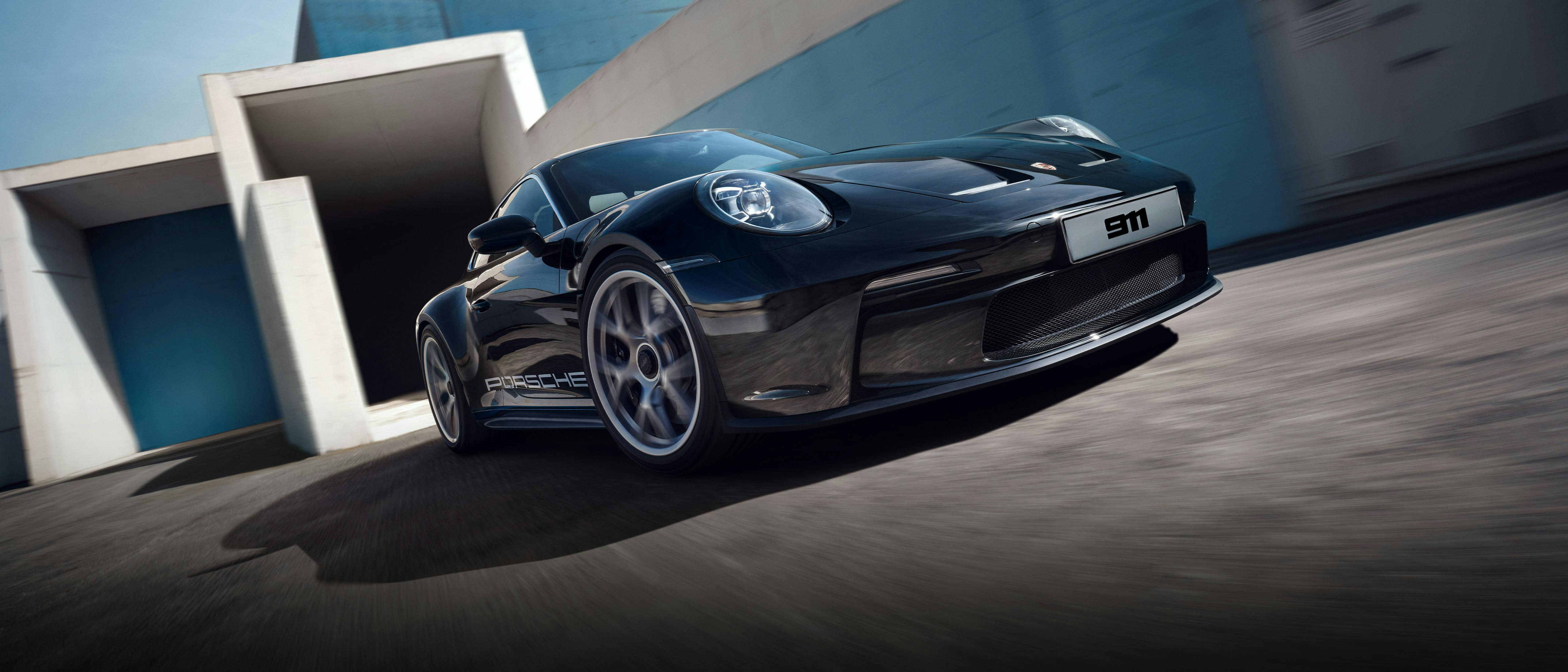A sleek black Porsche 911 sports car with aerodynamic design and bold detailing, captured in motion near a modern architectural backdrop.