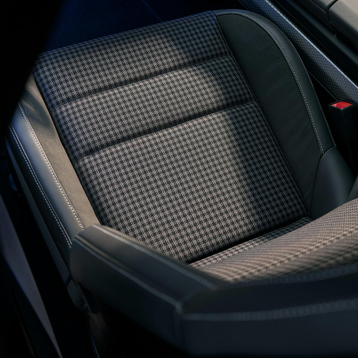 Close-up of a Porsche car seat featuring a houndstooth-patterned fabric in the center, surrounded by black leather with visible white stitching, showcasing a blend of classic and modern design elements.