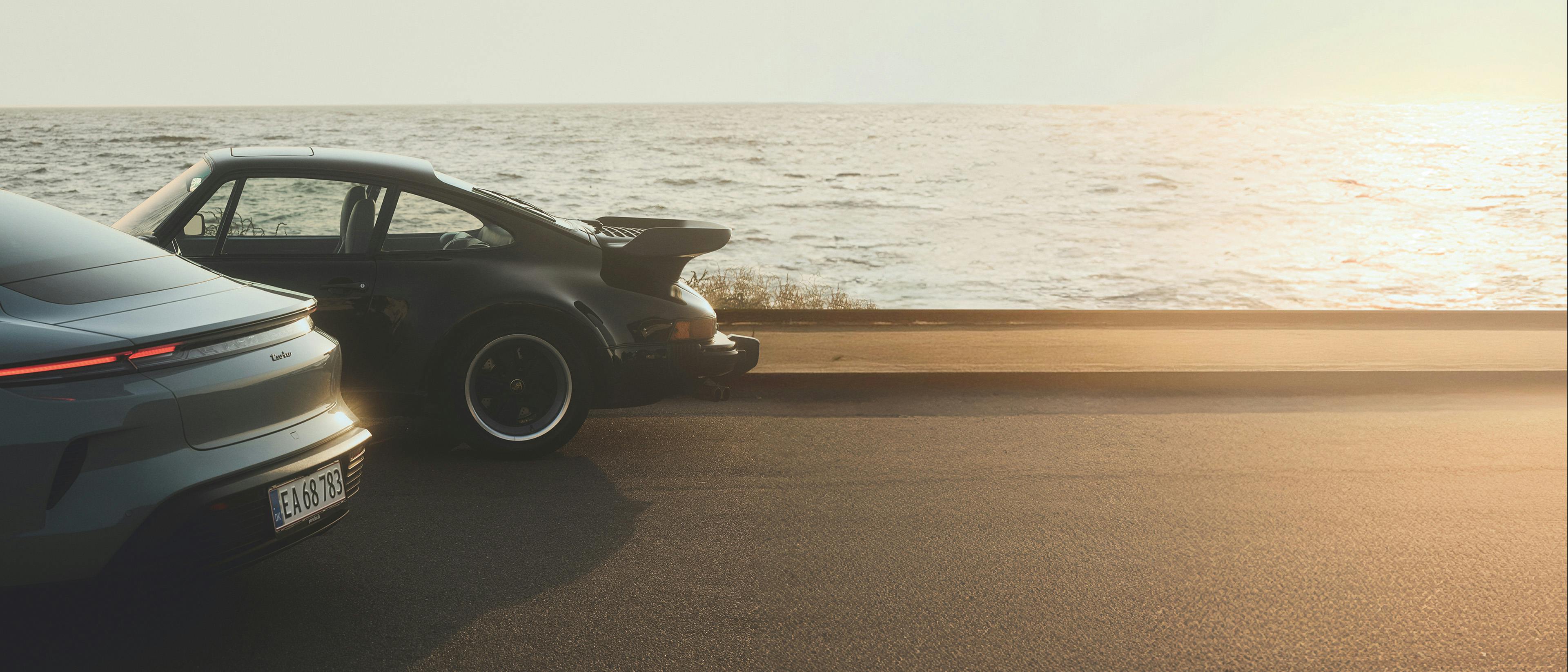 Une Porsche Taycan Turbo et une 911 sur une route côtière au coucher du soleil, au bord de la mer.