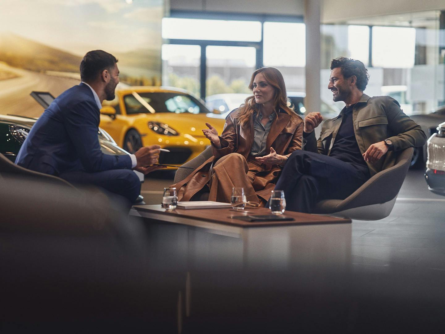 A couple during a consultation in the Porsche center, various Porsche vehicles in the background.