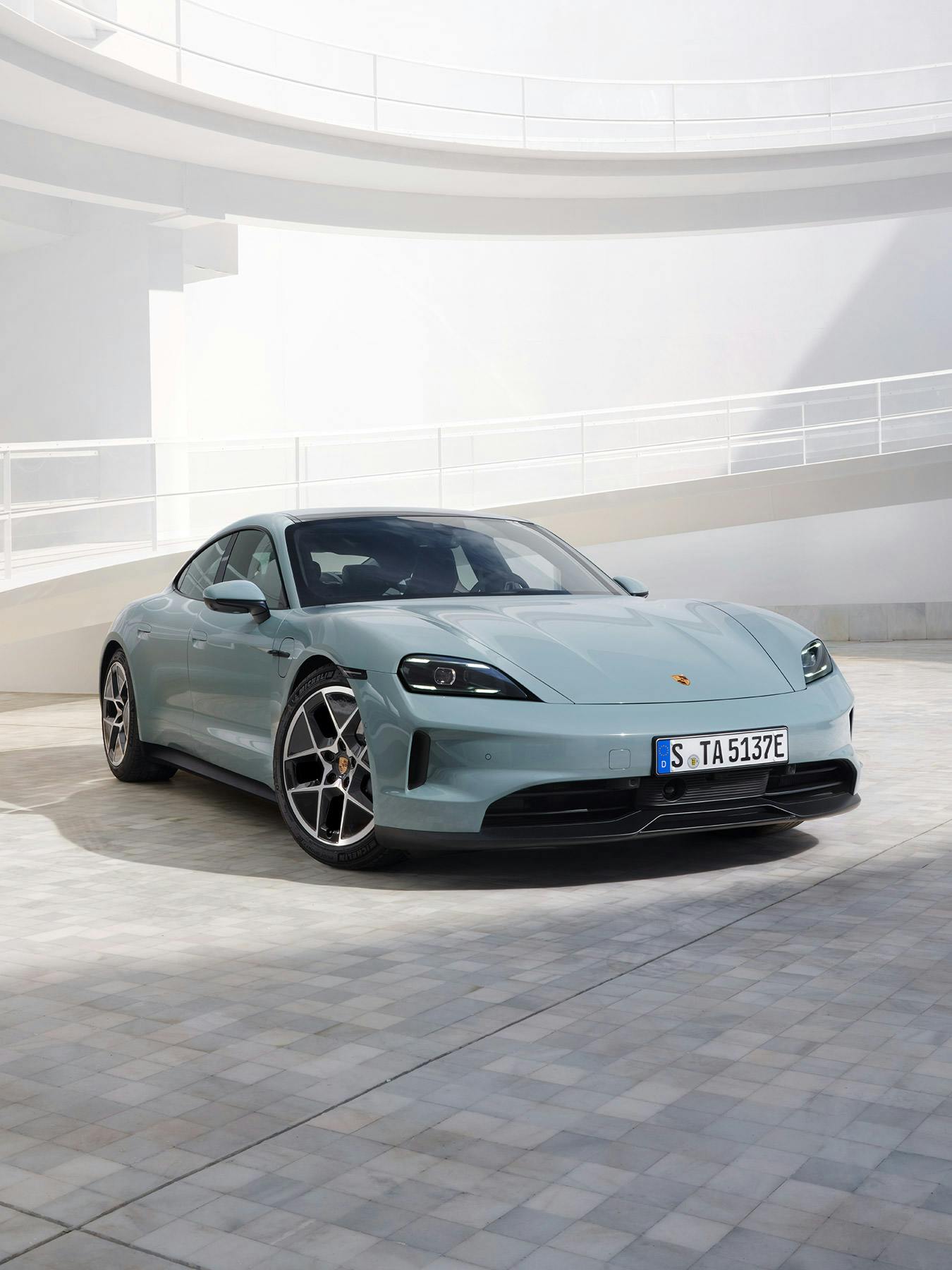 Un Porsche Taycan bleu clair au milieu d'une cours intérieure.
