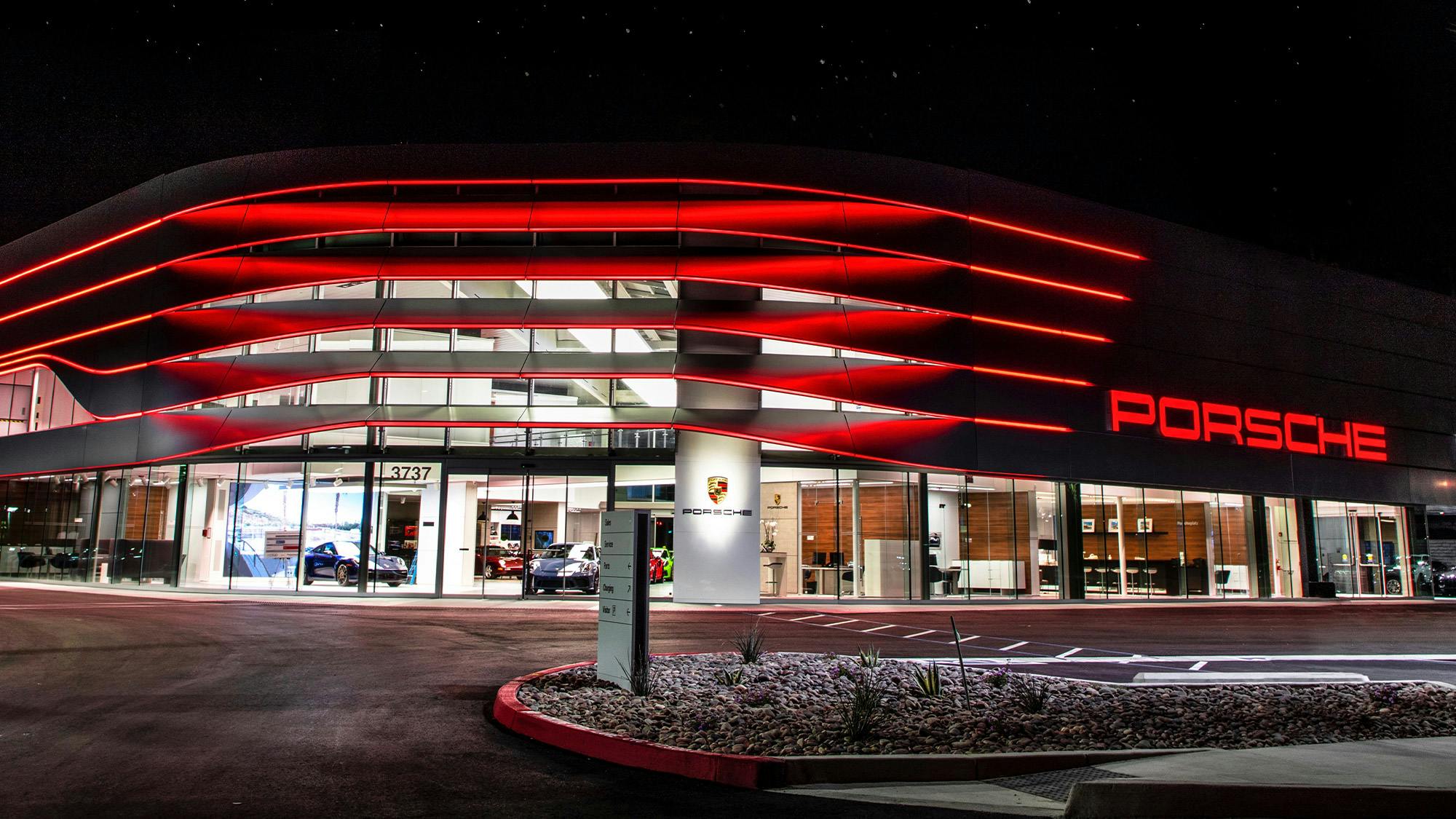 The Porsche center's main entrance in the evening with modern, red exterior lighting.