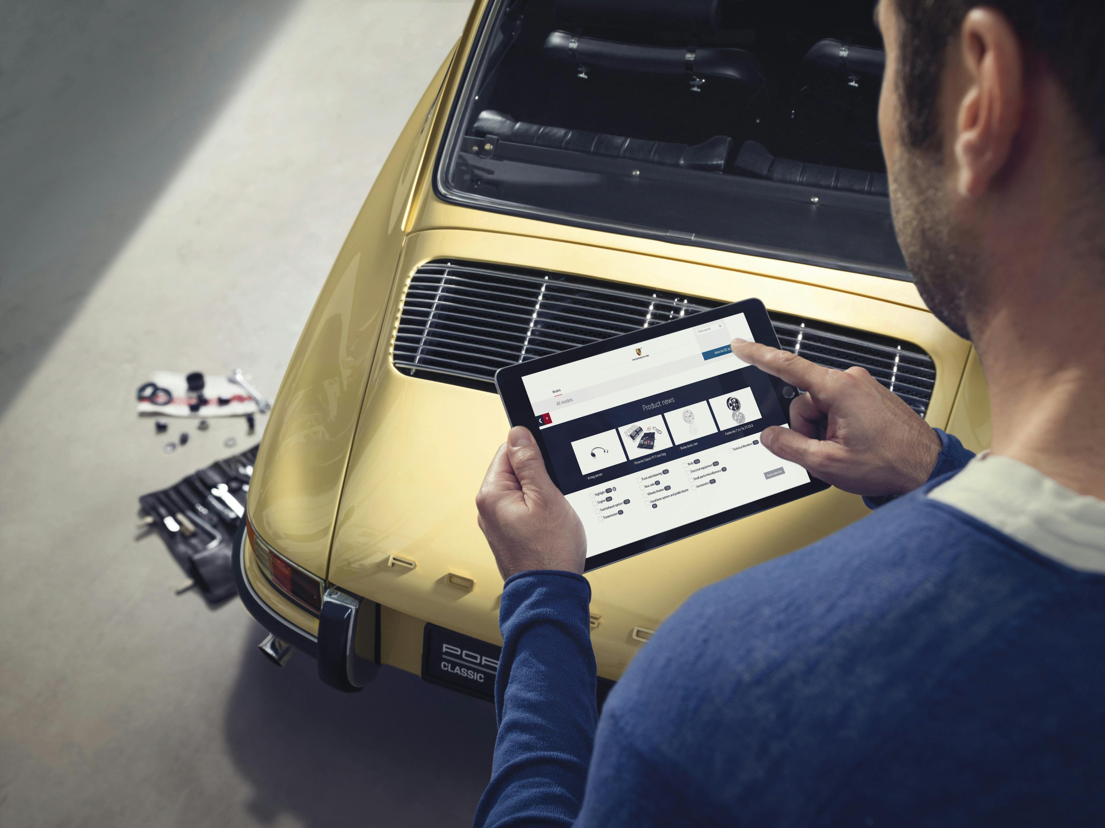 A man is holding a touchpad with the Porsche Classic Parts Explorer open.