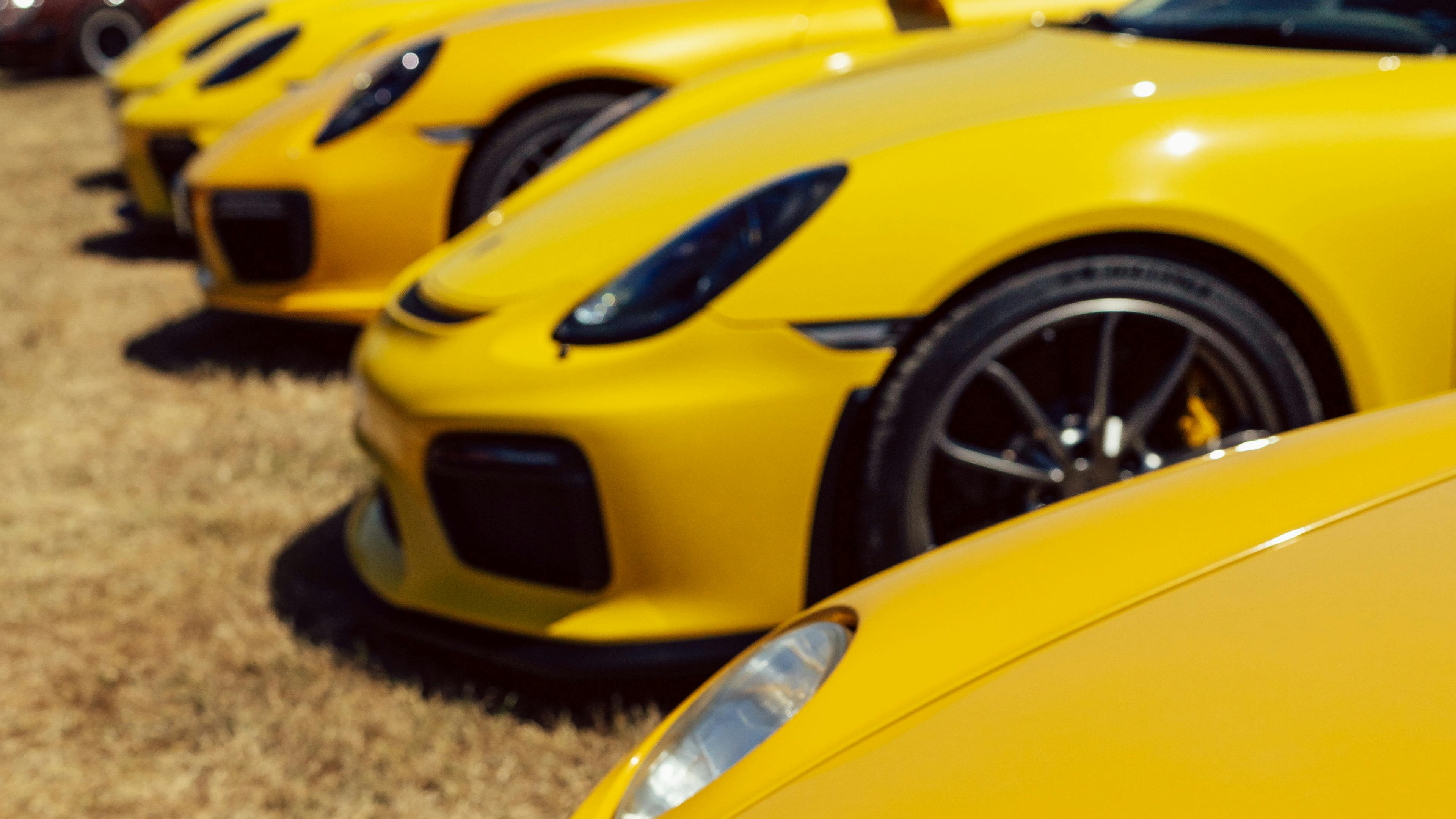 Close-up of a row of yellow Porsche 911 GT3s and GT4s parked side by side, headlights and wheels in focus.