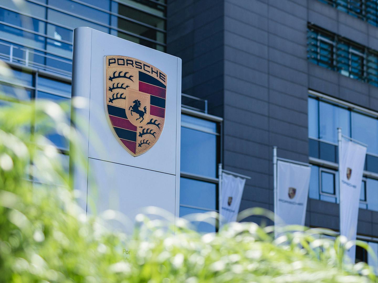 Porsche in Bietigheim-Bissingen, Firmengebäude mit Porsche Logo und Porsche Flaggen drumherum.