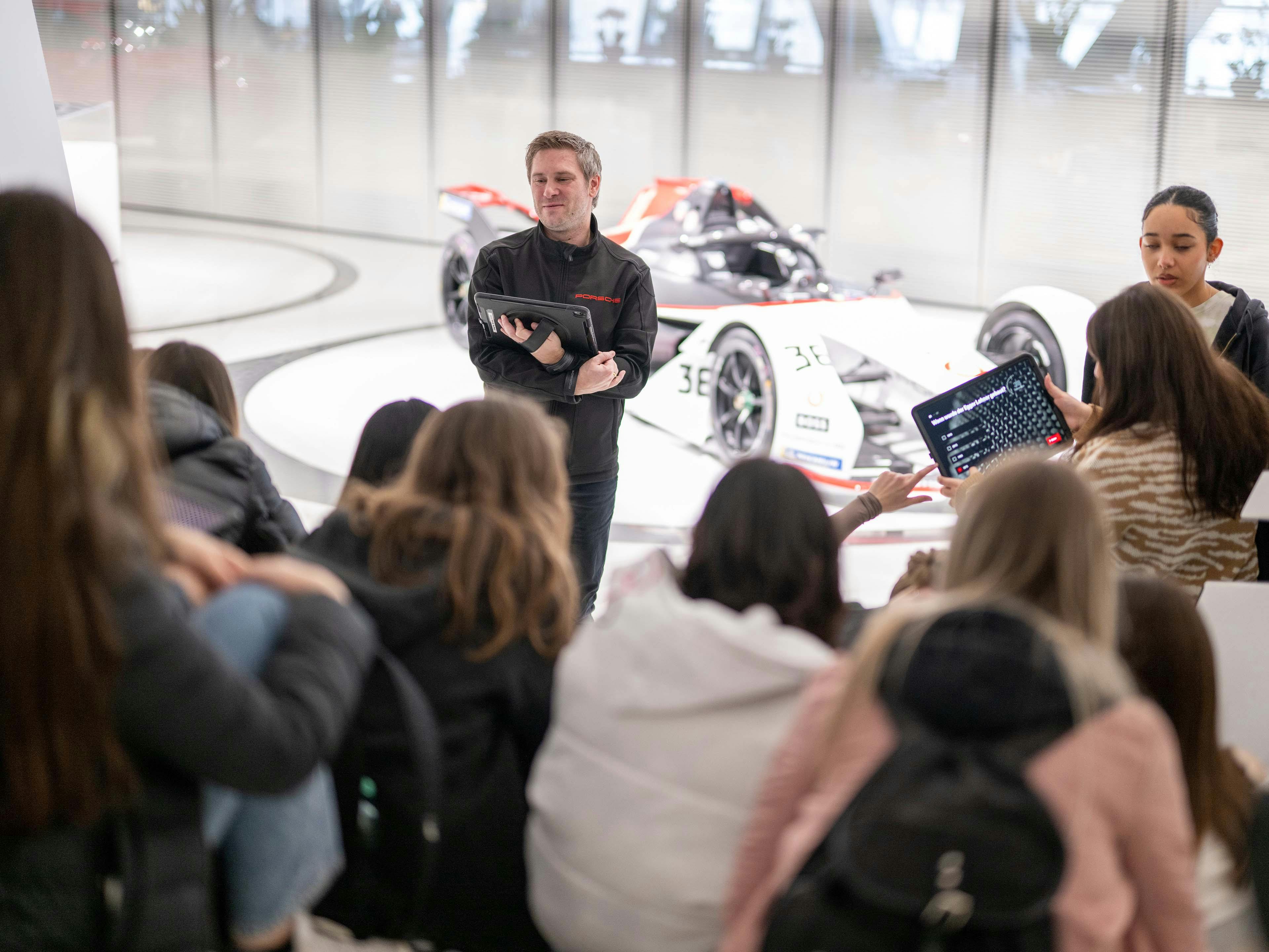 Einer Gruppe Schüler wird die Vorteile von Leichtbau und Aerodynamik anhand des Porsche Formel-E Fahrzeugs erklärt.