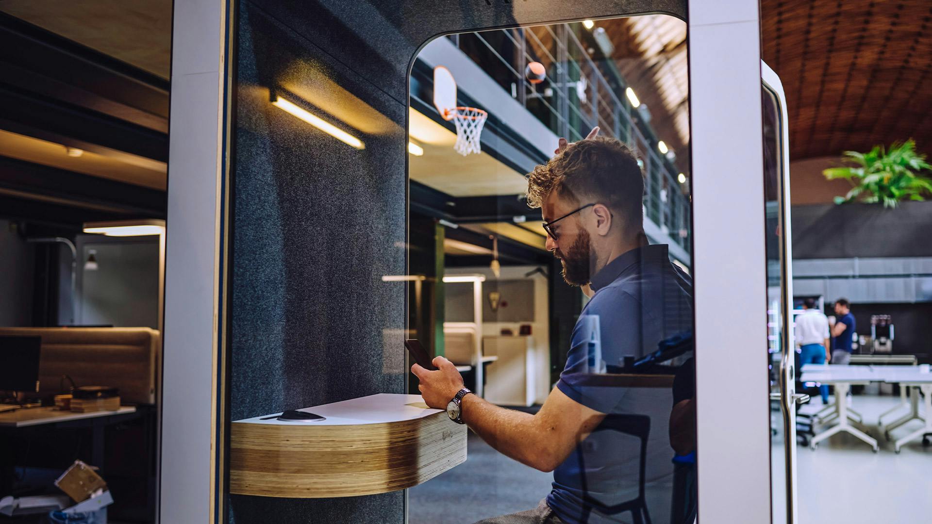 An office at Porsche: a man is sitting in a phone booth, typing intently on his mobile phone.