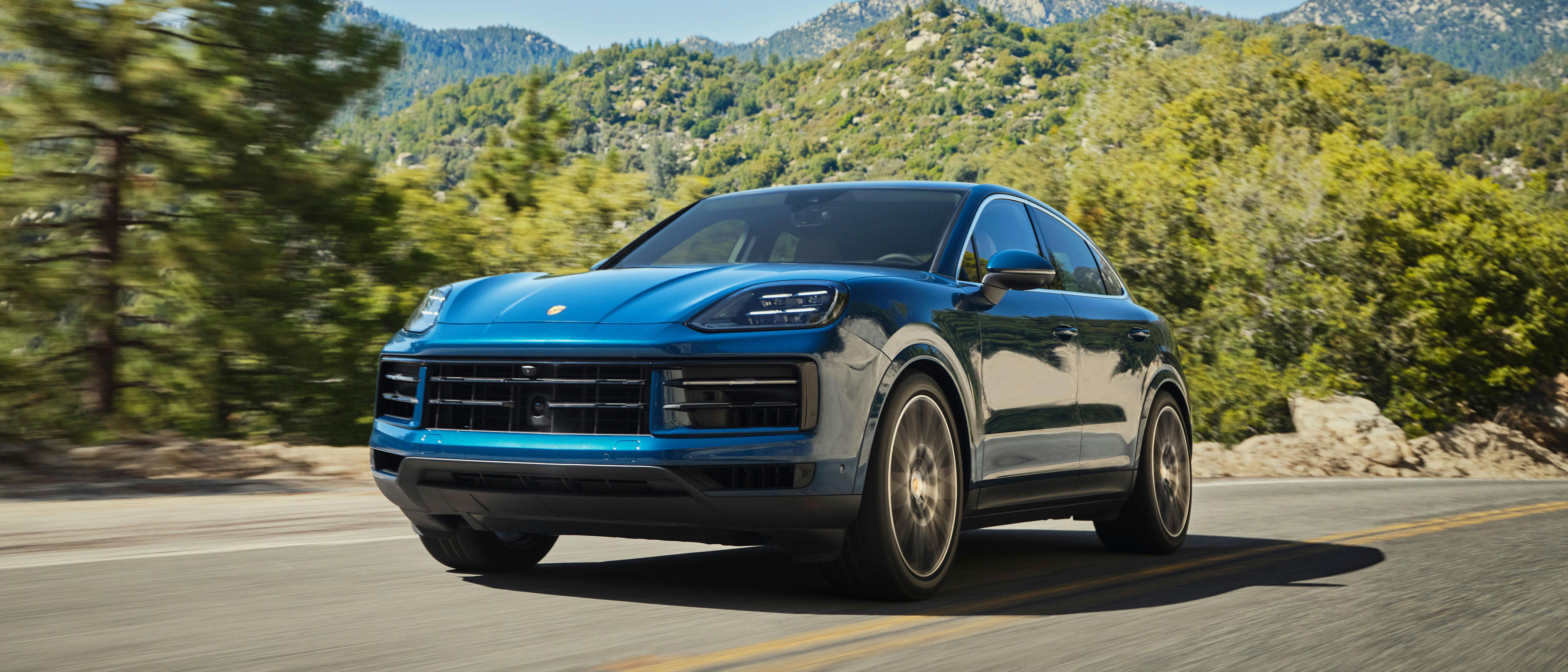 A blue Porsche Cayenne driving along a mountainside road.