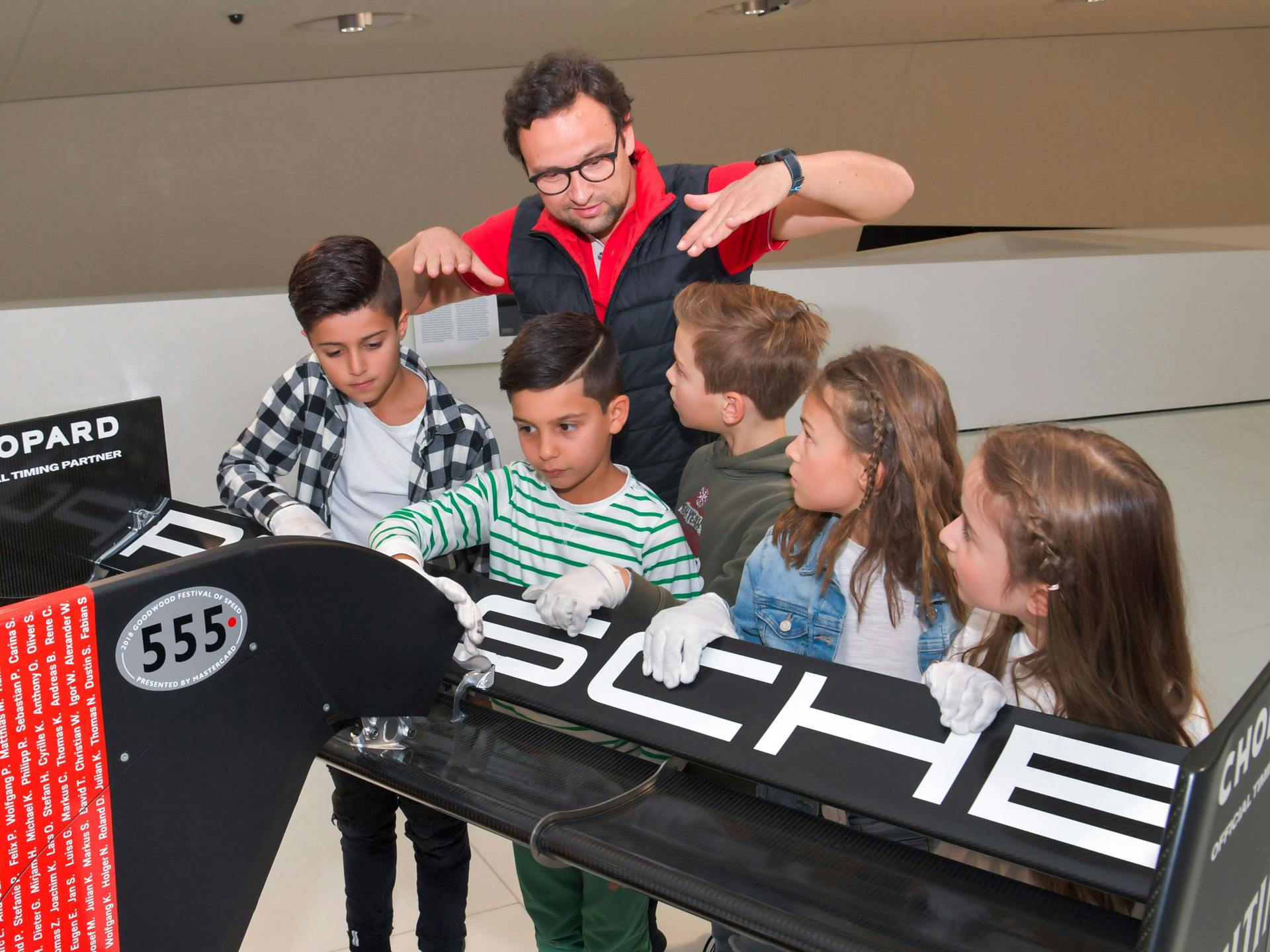 A group of children and a Porsche Museum employee standing at the rear of a Porsche