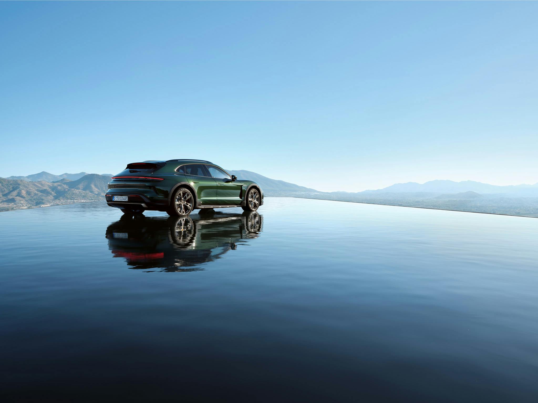 A green Porsche parked on a reflective surface with mountains and a clear sky in the background.