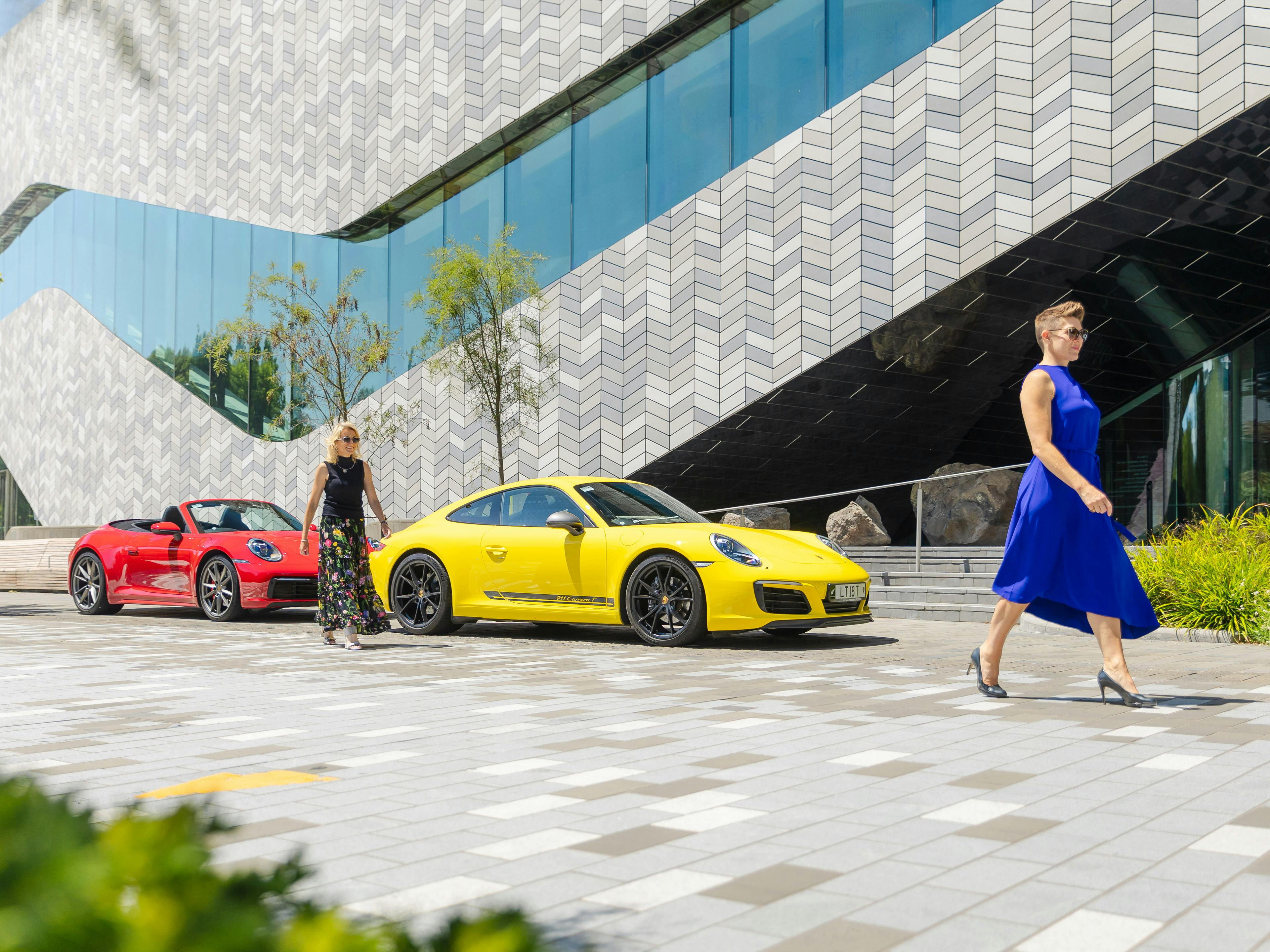 Sarcha and Leanne walking confidently alongside their Porsche cars
