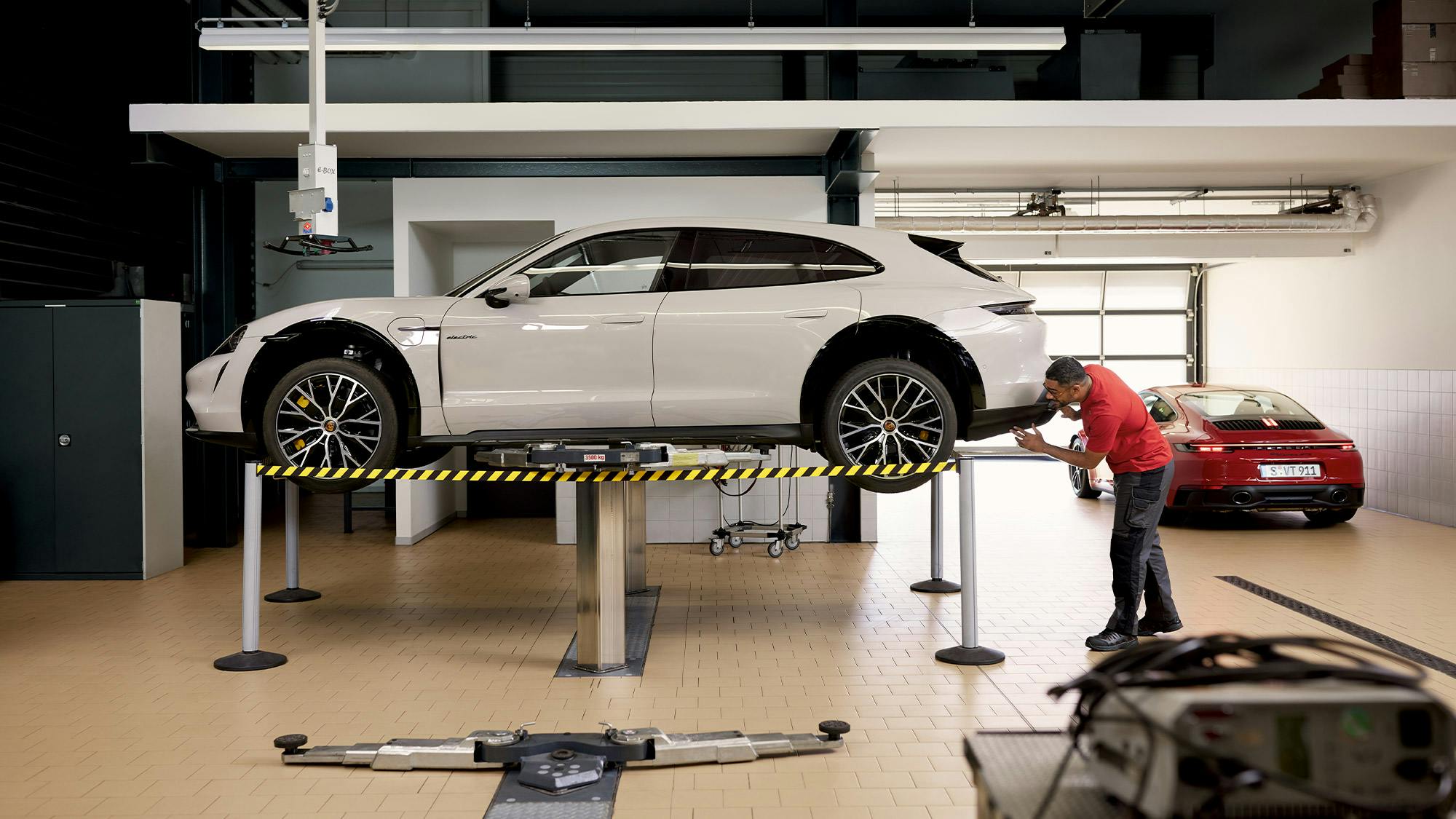 Un técnico revisa un Porsche Taycan en color Blanco situado sobre una plataforma elevadora.