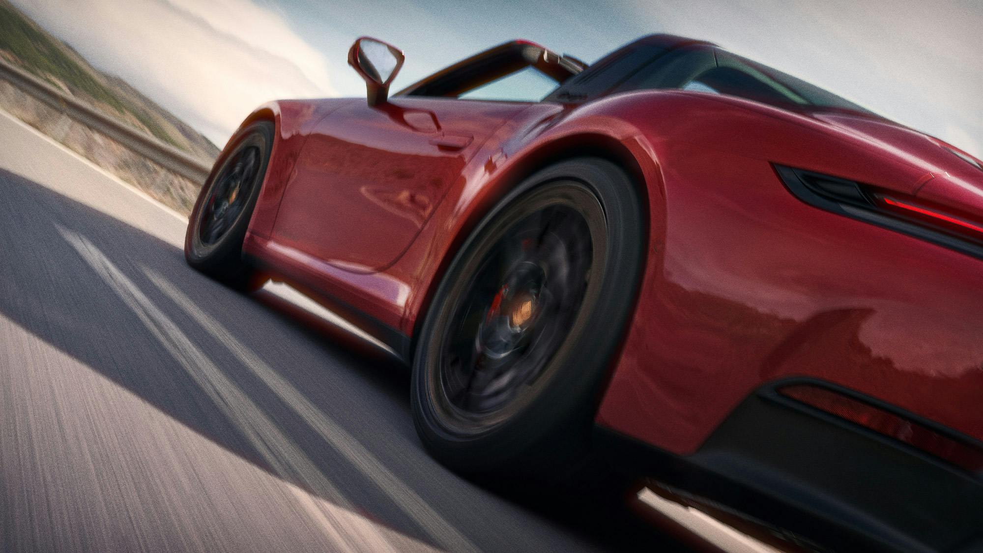 Vue arrière en contre-plongée d'une Porsche 911 rouge roulant sur une route de montagne sinueuse.