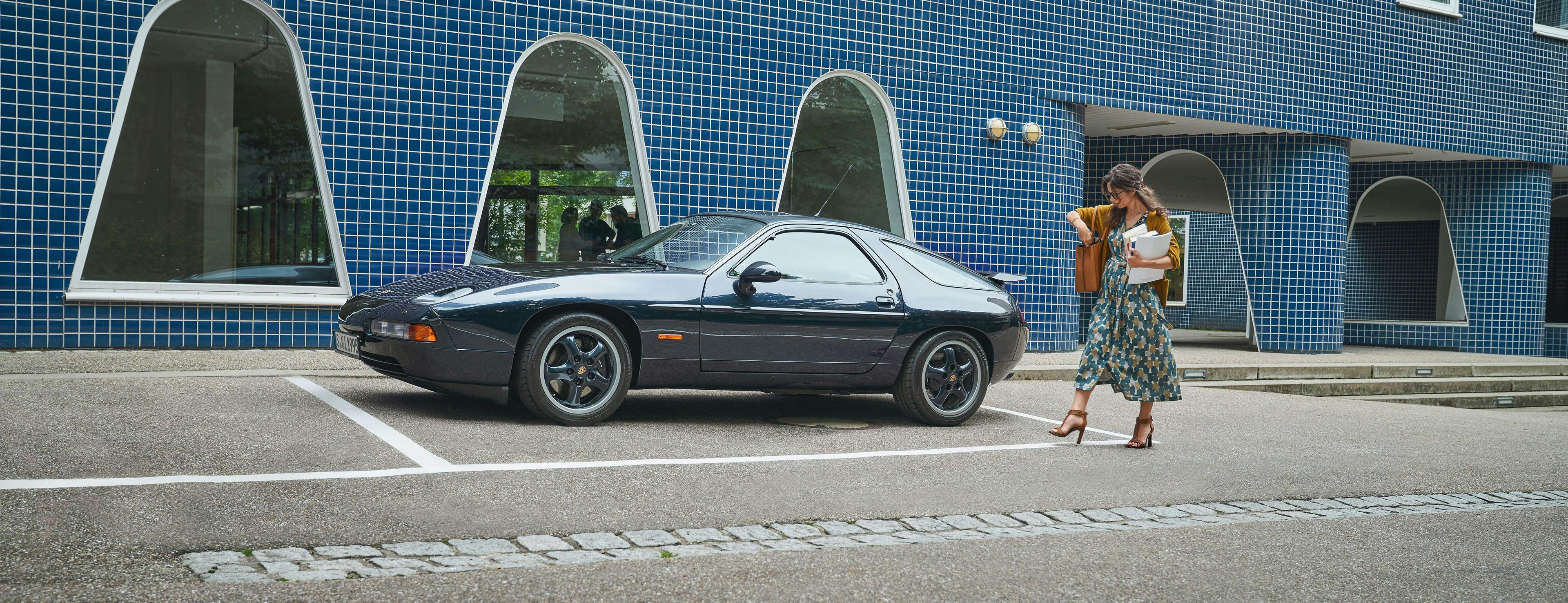 Street scene with Porsche 928 parked in front of blue house.