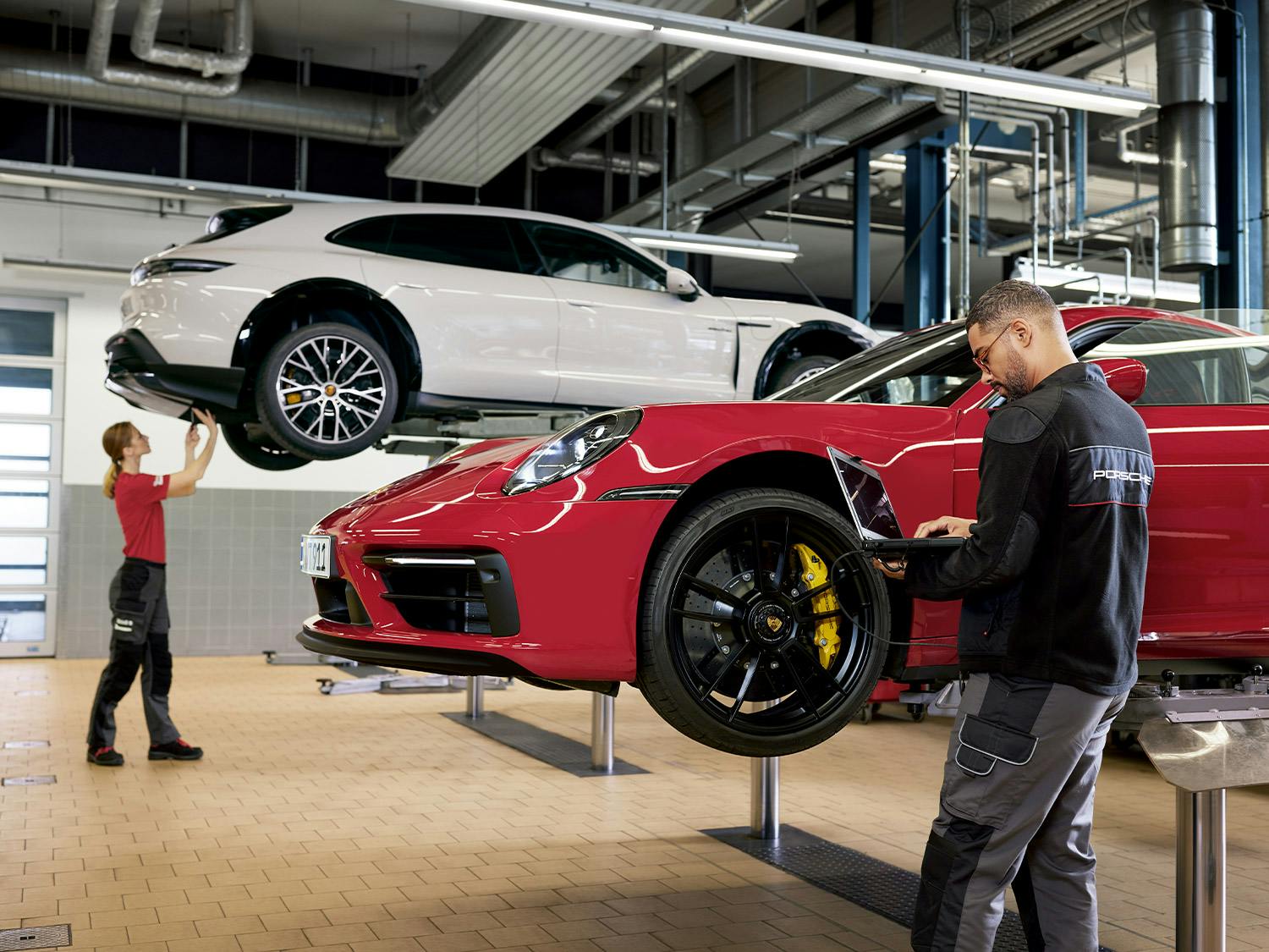 Ein Porsche-Automechaniker mit Tablet in der Hand inspiziert ein Porsche auf einer Hebebühne in einer Werkstatt.