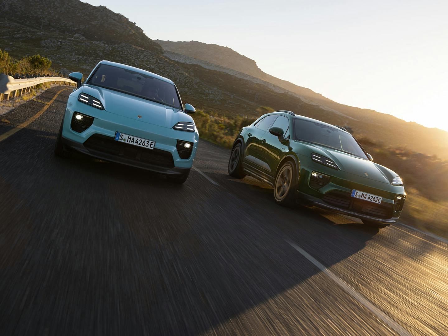 Twee porsches rijden naast elkaar op de weg met zonsondergang, er zijn bergen op de achtergrond