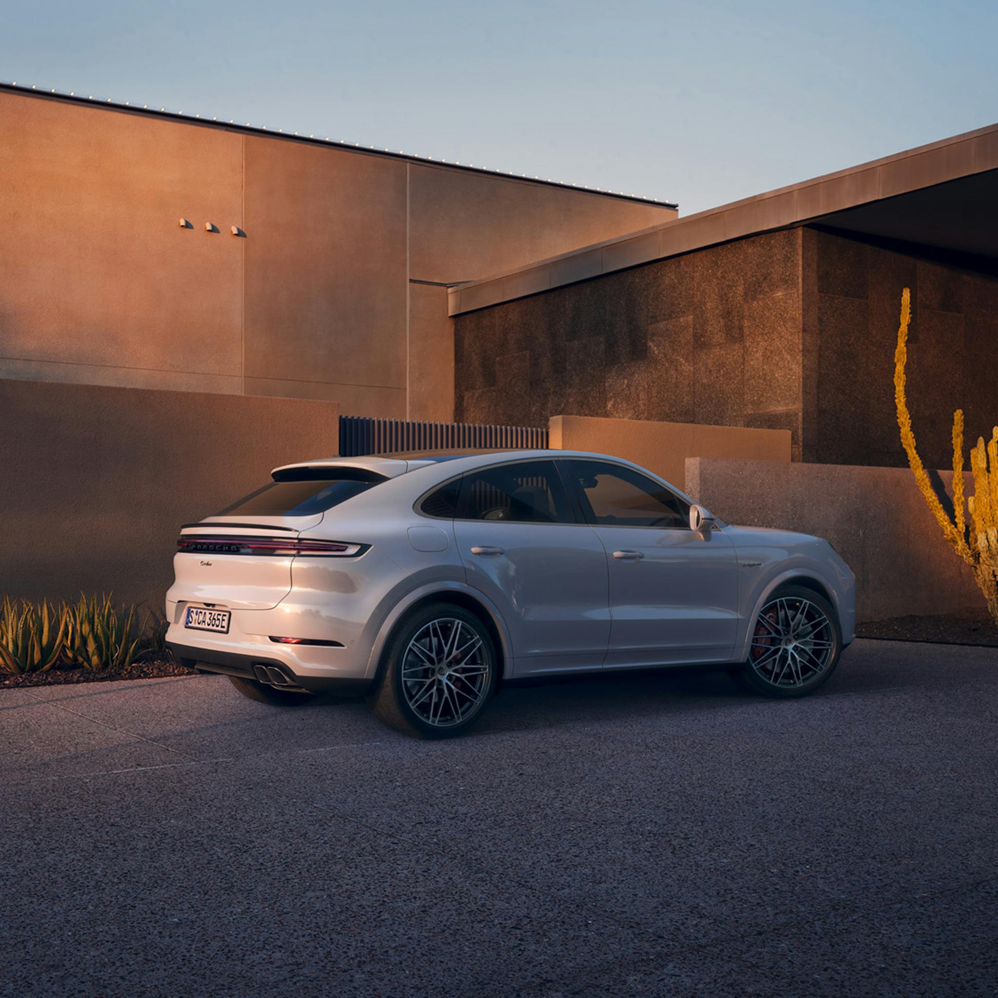 Rear three-quarter view of a white Porsche Cayenne parked beside a modern concrete building at dusk.