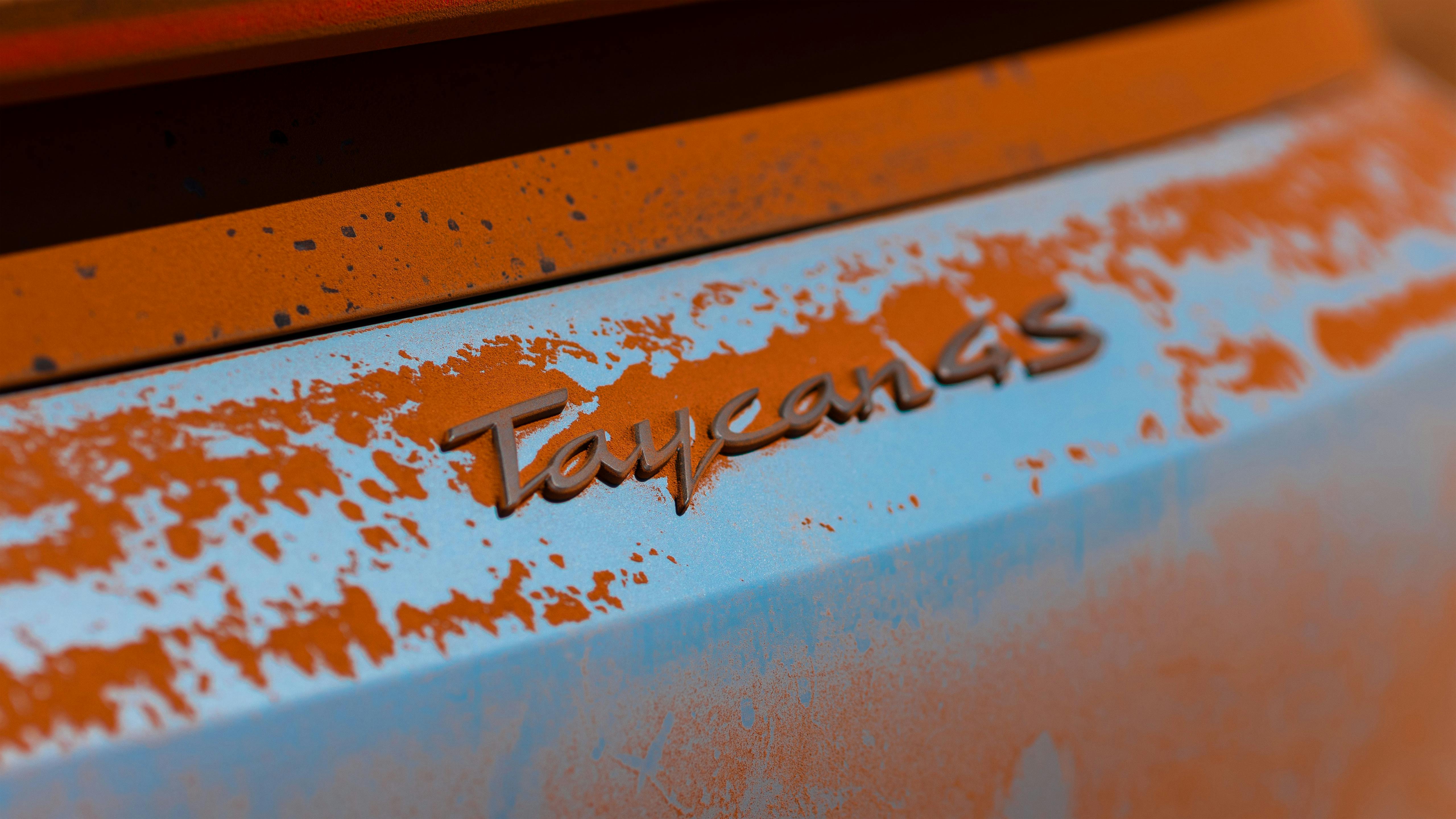 Porsche Taycan 4S badge closeup surrounded by red dirt