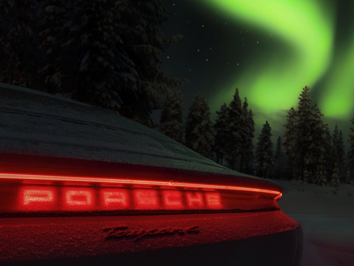 View of the taillights of a Porsche Taycan at night, with a green aurora borealis in the night sky in the background.