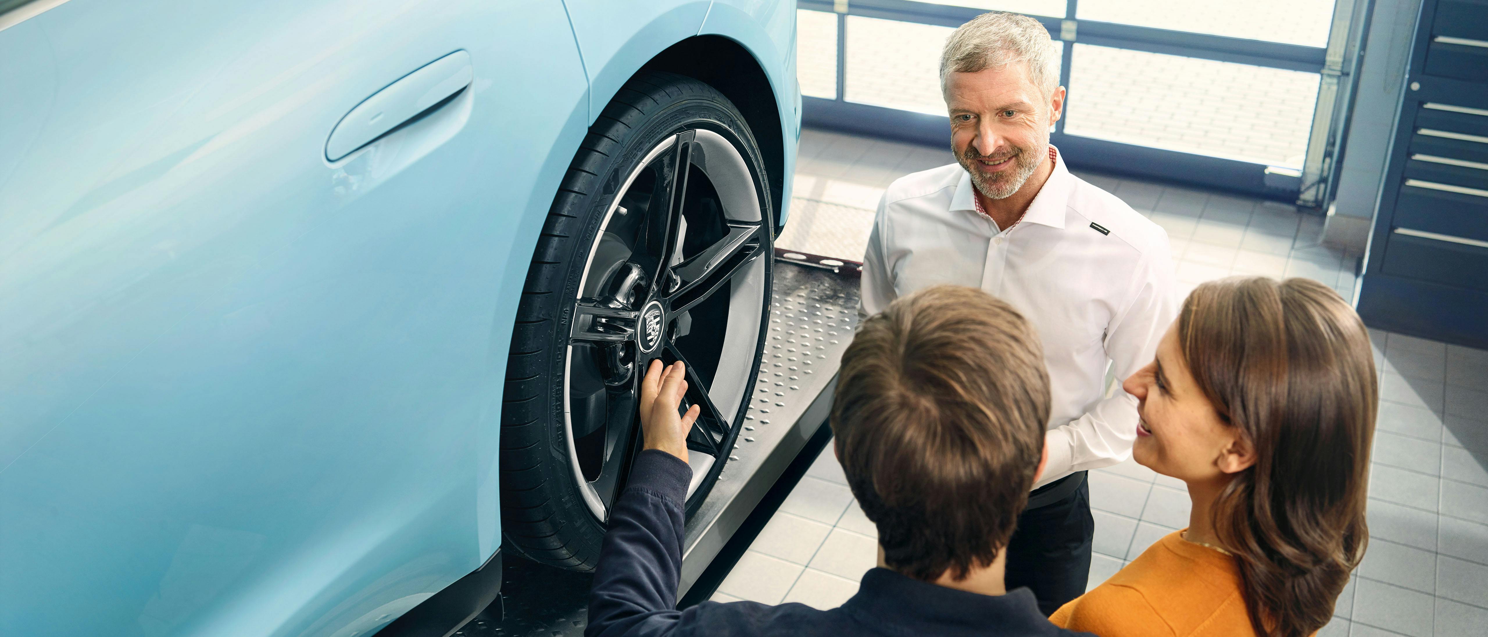 Ein Porsche Zentrum Mitarbeiter und zwei Kunden stehen bei einem Fahrzeug und sind im Gespräch.