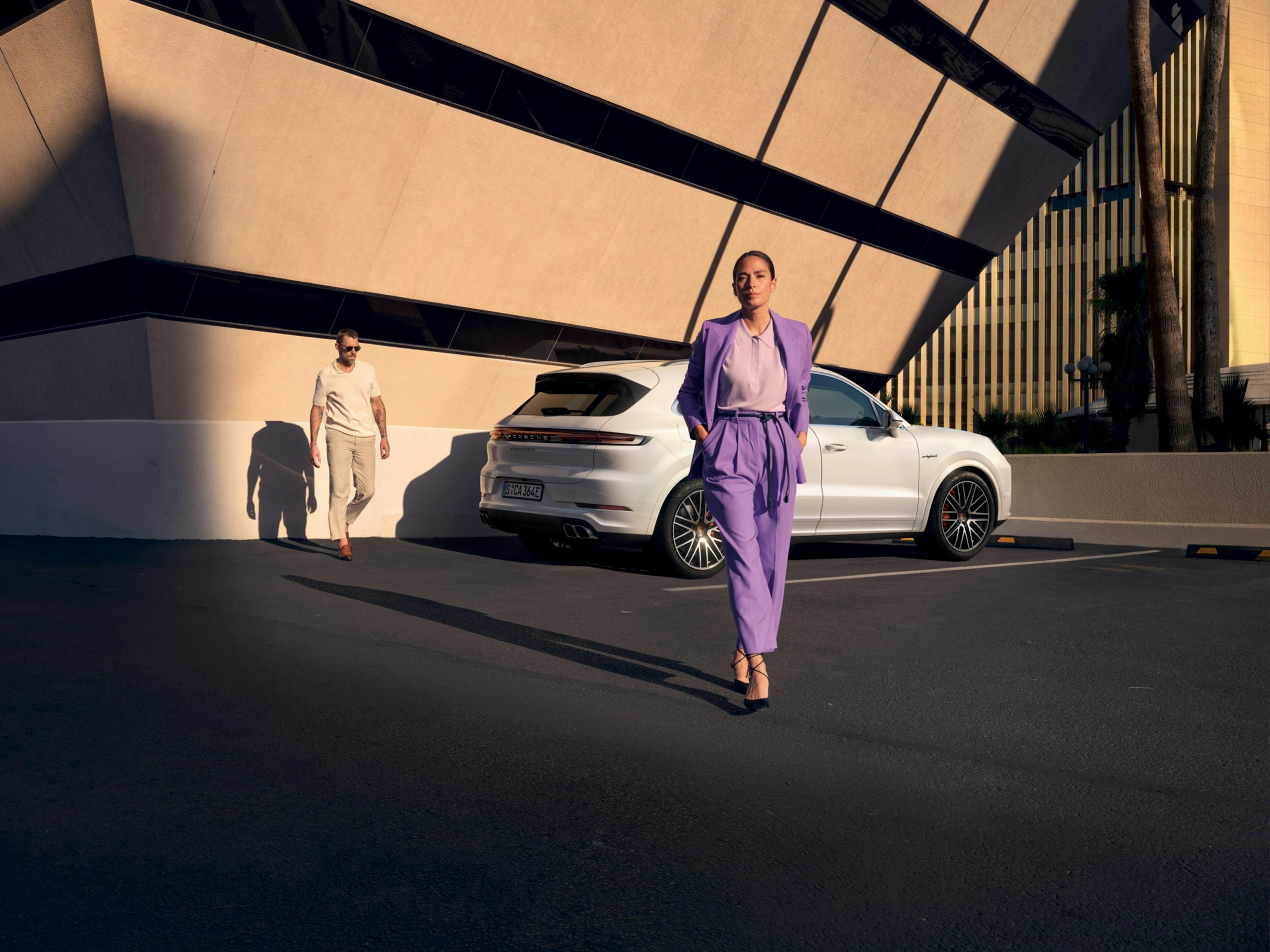 Rear shot of a white Cayenne Turbo E-Hybrid standing nect to a modern building at sunset with two young people in the foreground