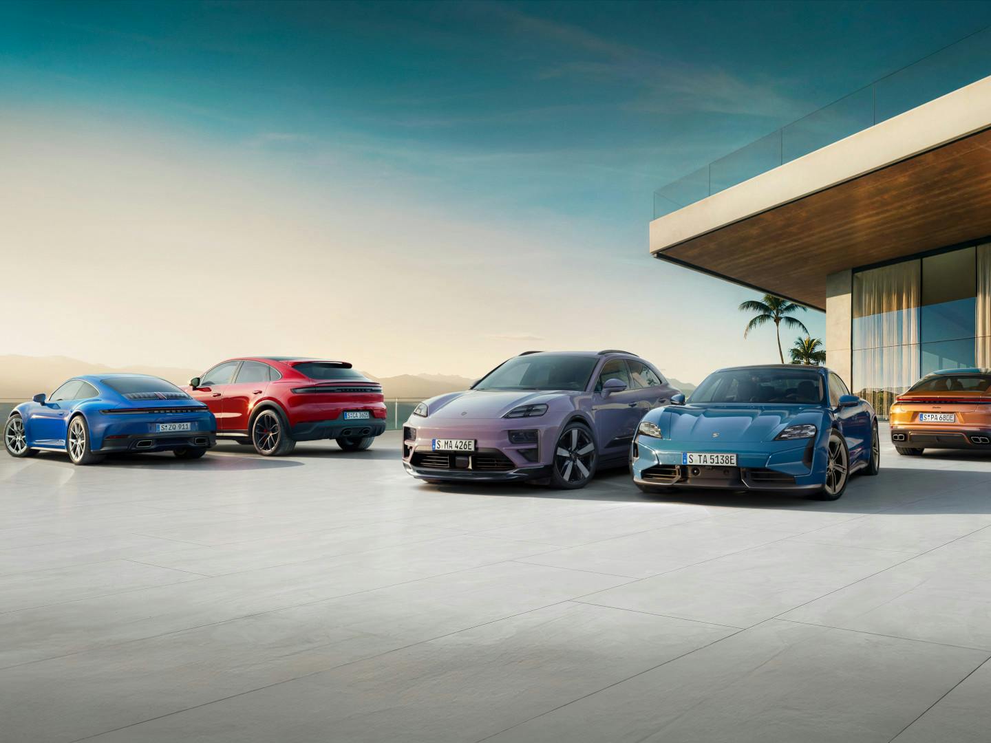 Cinque veicoli elettrici e ibridi Porsche sono affiancati uno accanto all’altro davanti a un’architettura moderna, in un ambiente soleggiato.