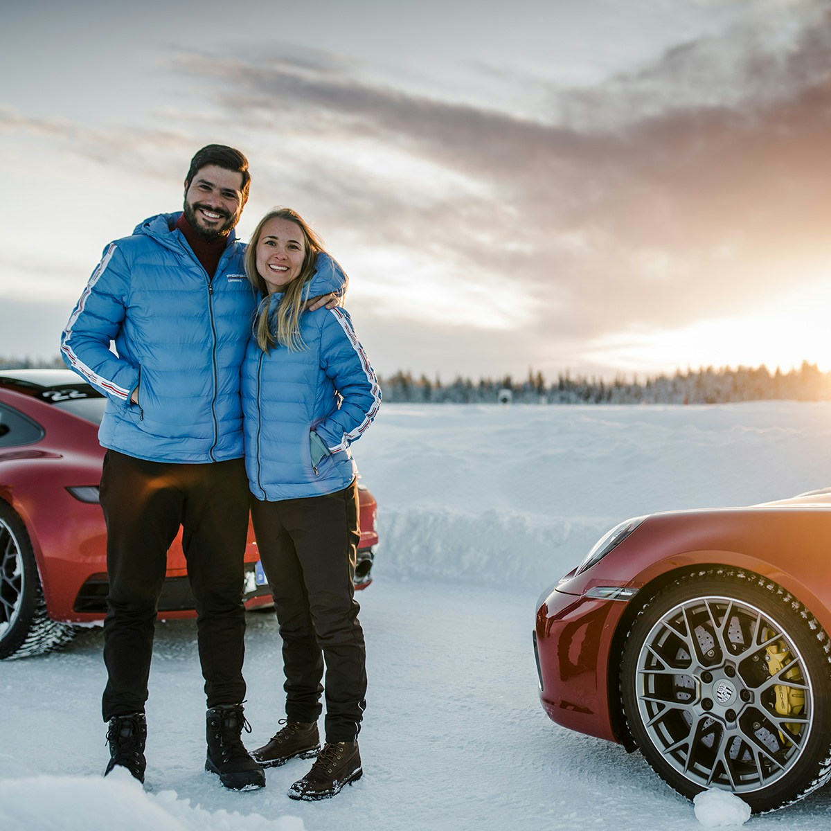 Ein fröhliches Paar im Schnee, mit einem Porsche im Hintergrund.