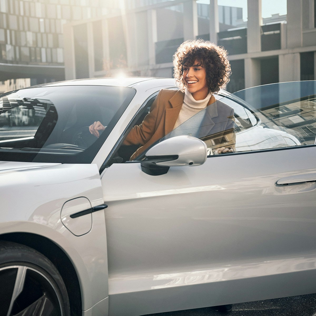 A woman partially outside of a Porsche car.