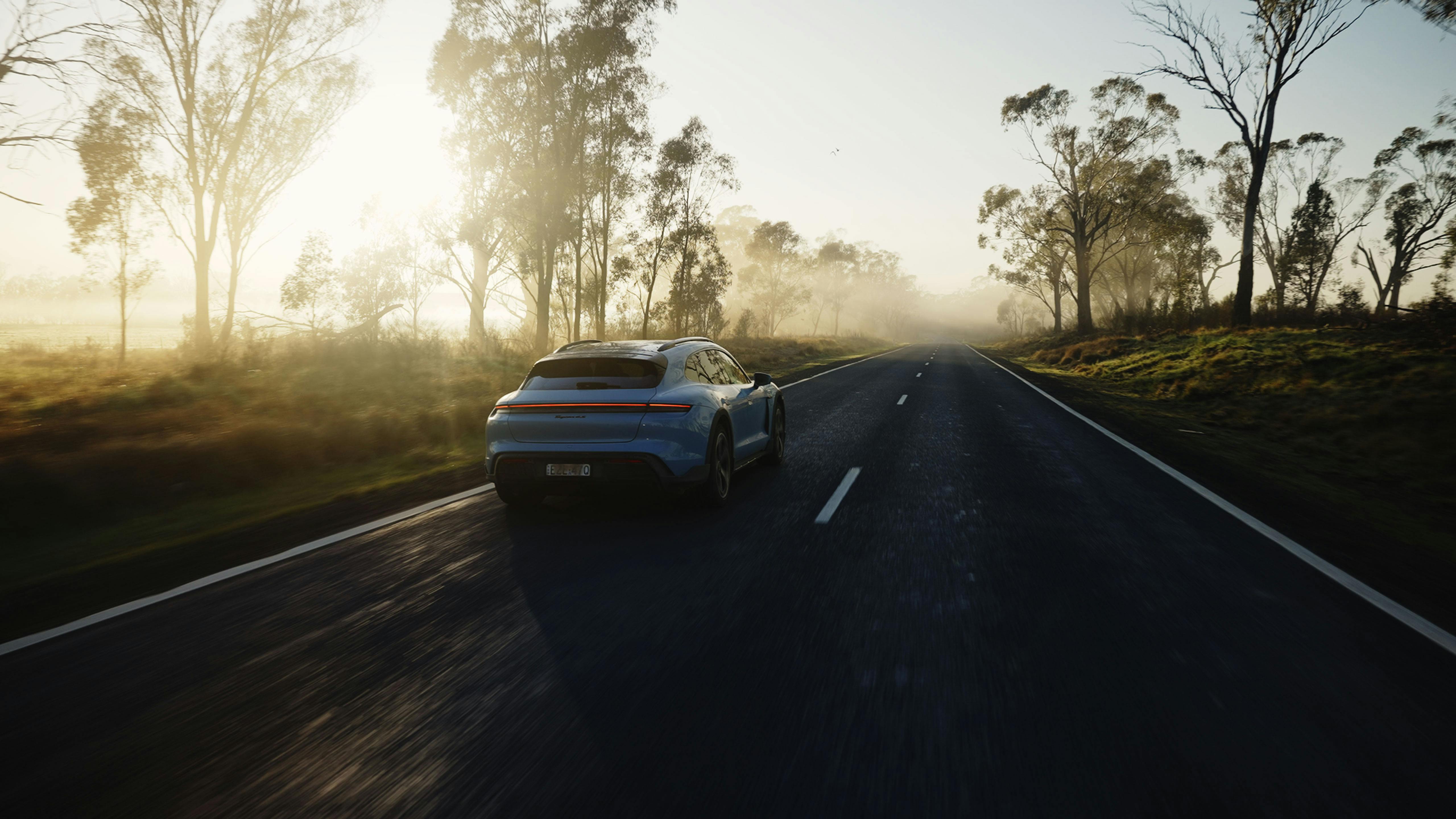 Porsche Taycan driving on a misty road at sunrise