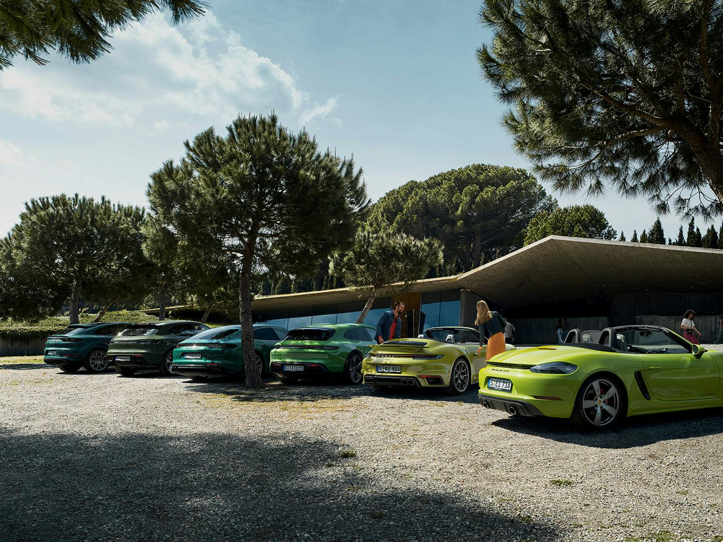 Mehrere Porsche‑Modelle – 718 Boxster, 911 Turbo, Cayenne Turbo, Panamera Executive, Panamera Turbo und Taycan Cross Turismo – stehen in einer Reihe auf einem kiesbedeckten Platz.