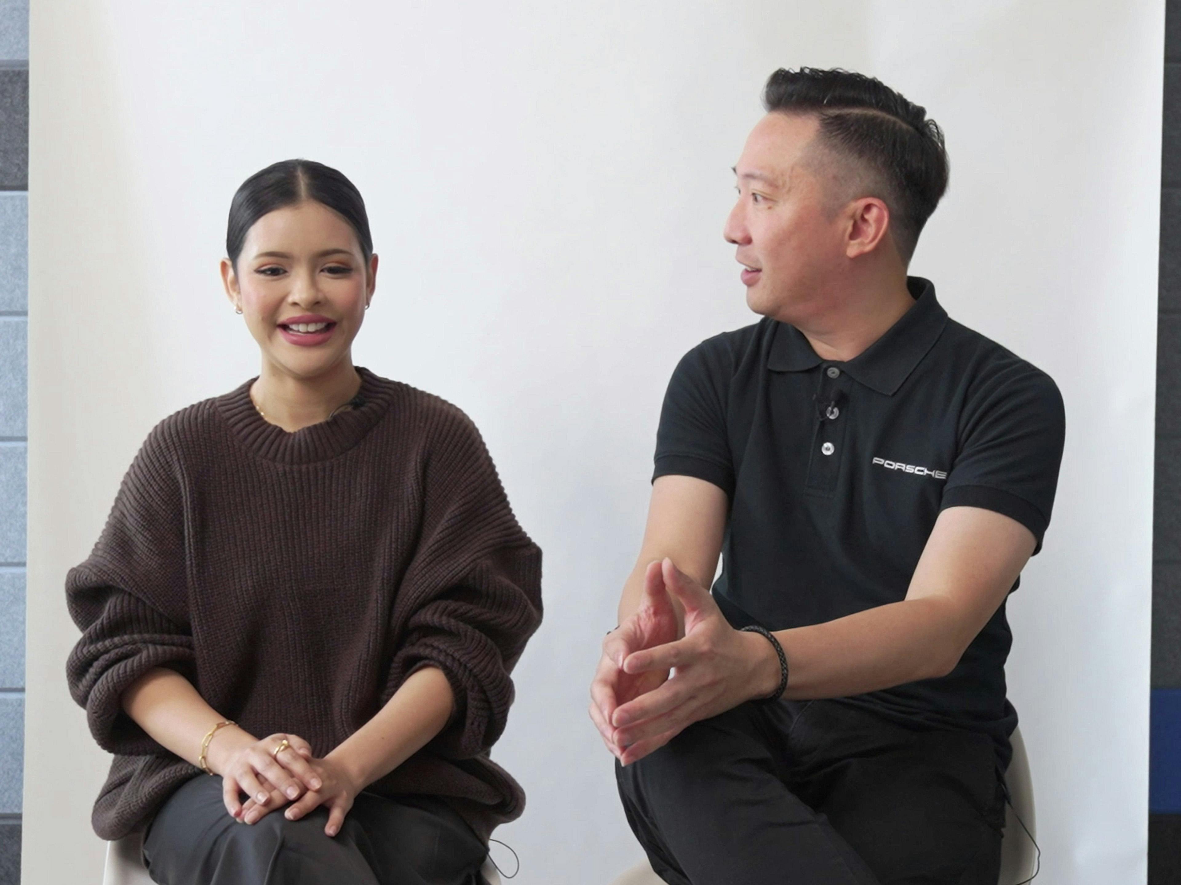 Porsche employees Wanie and Andrew sitting in front of the camera in an interview and talking with each other.