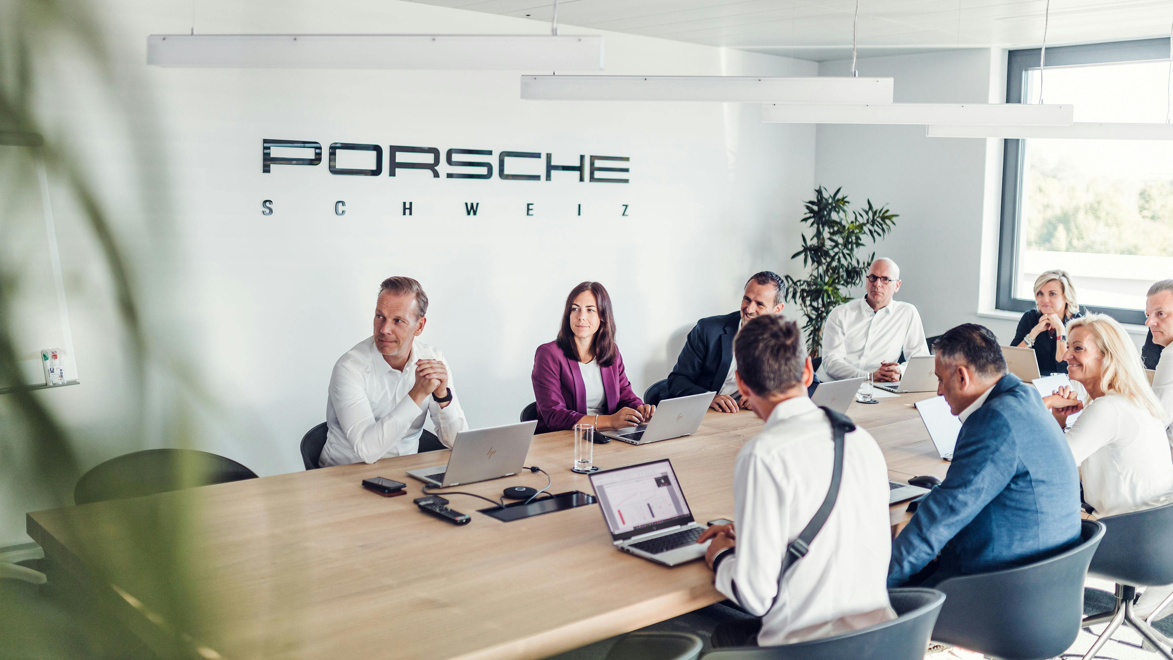 Eine Gruppe von Mitarbeitern der Porsche Schweiz AG sitzt an einem Tisch in einer Runde.