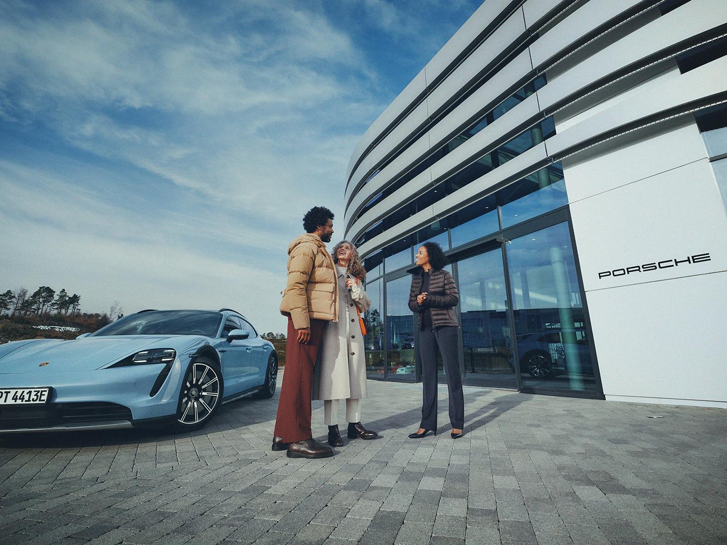 A female member of staff at a Porsche Centre speaking with customers outside.